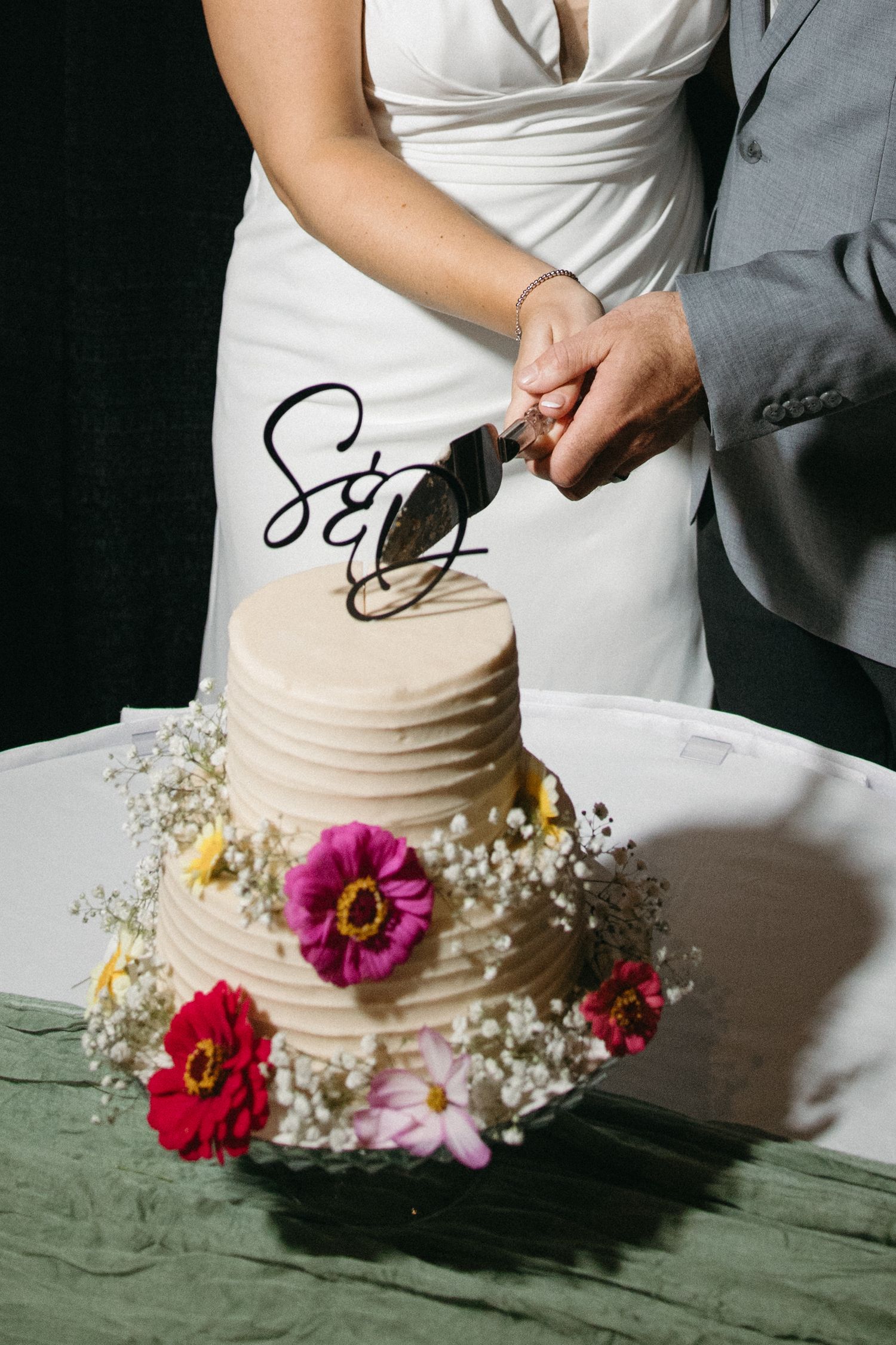 Wedding cake decorated with fresh pink and red flowers on a green tablecloth.