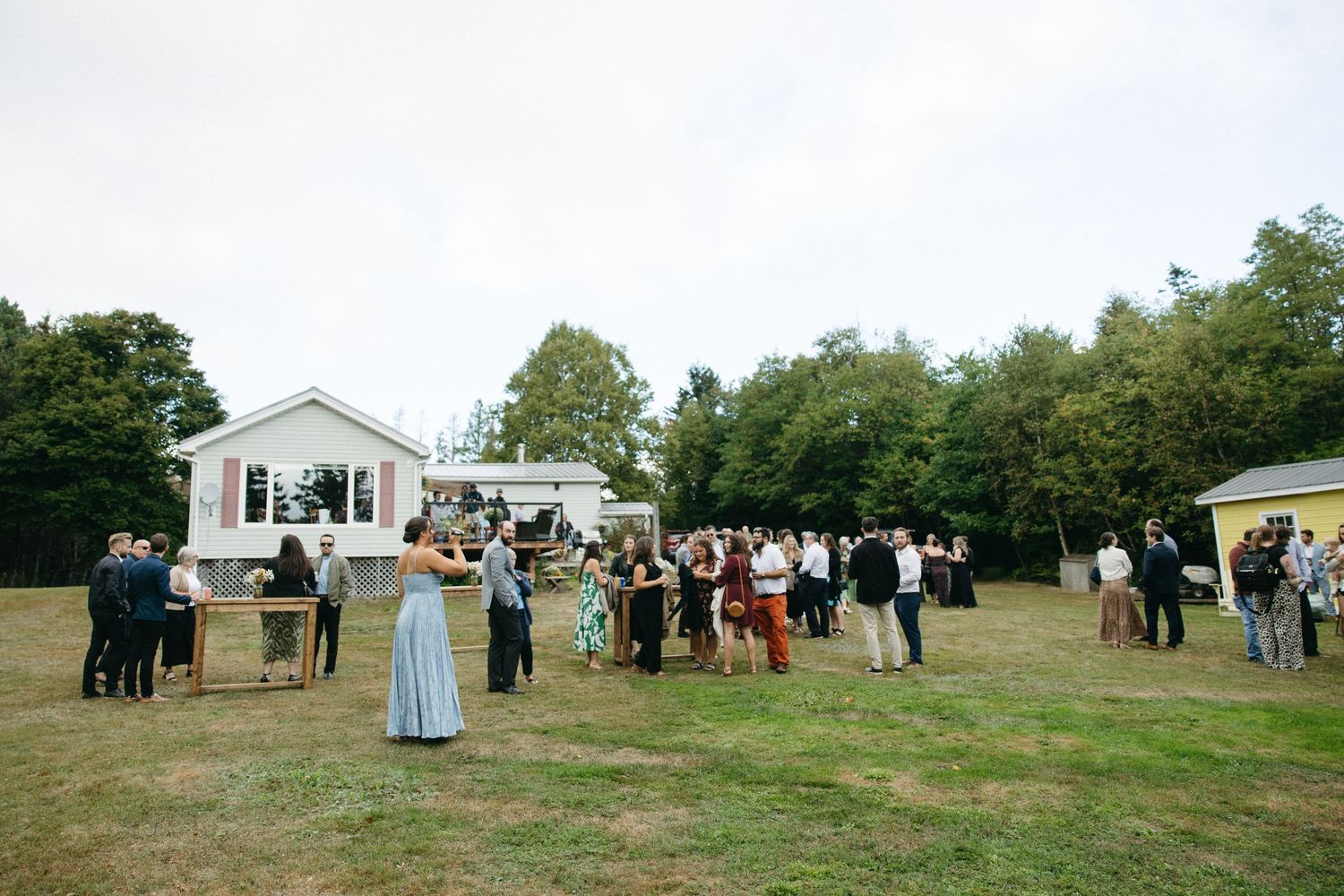 Wide shot of outdoor wedding reception with white building and scattered guests on lawn.