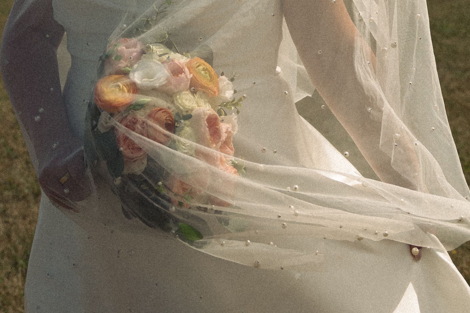 Close-up of bride holding a pastel floral bouquet through her flowing white veil outdoors.