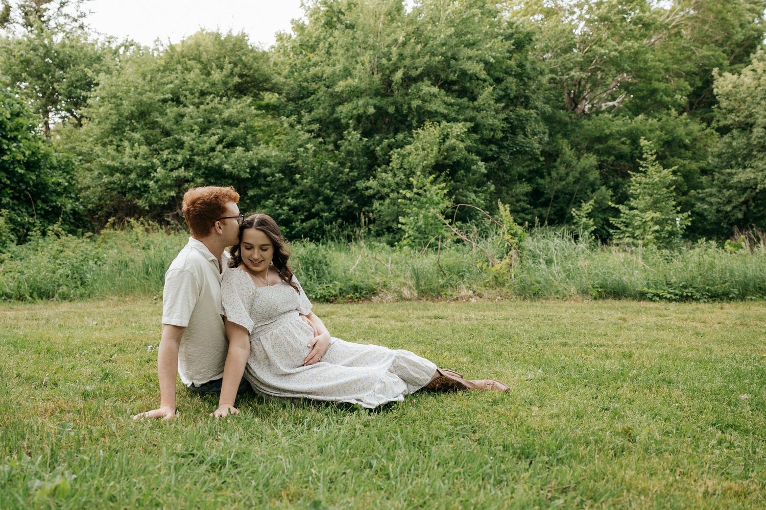 Two people relaxing in a serene meadow surrounded by lush greenery on a sunny afternoon.