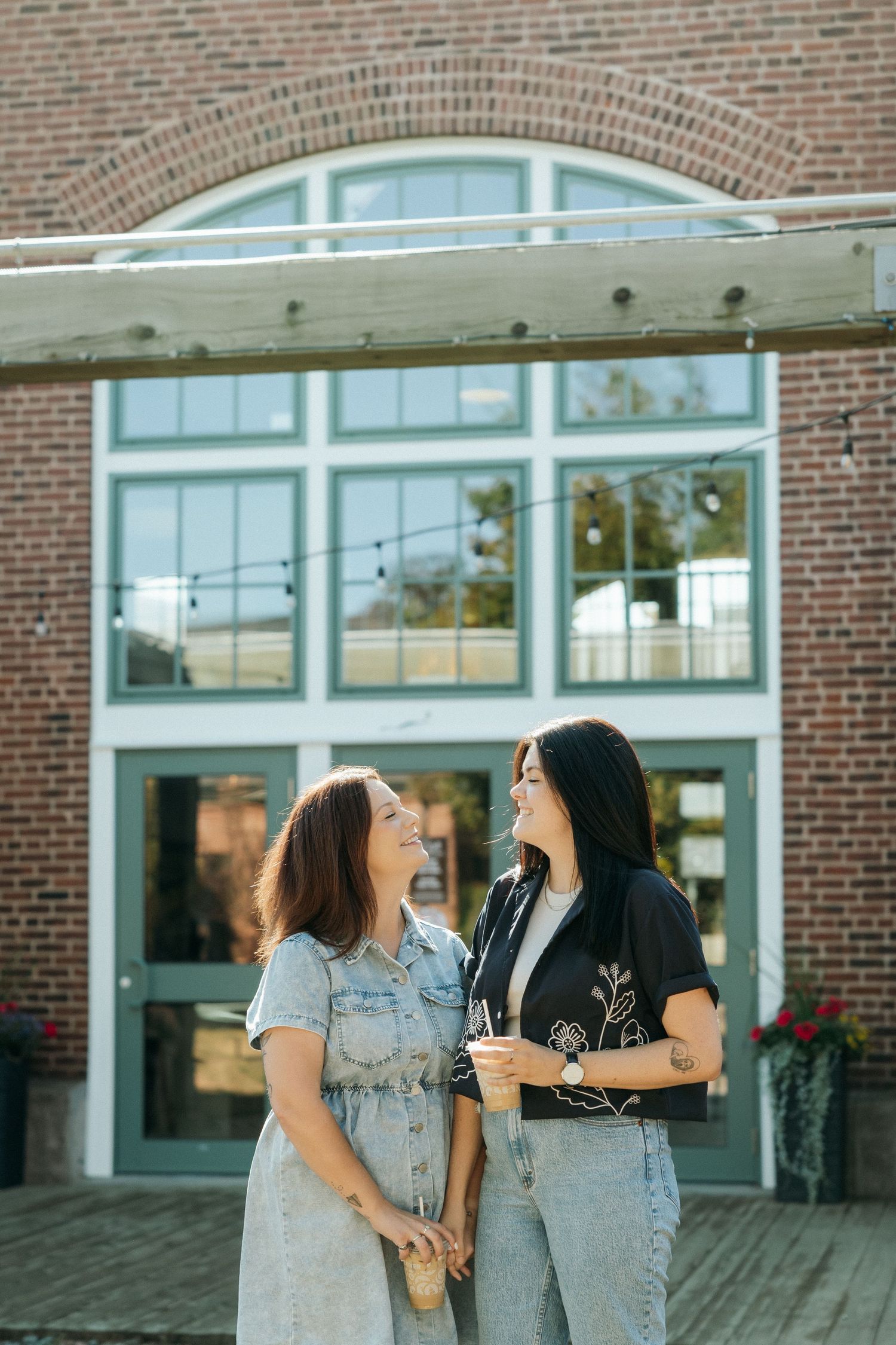Two people laughing together in front of a modern brick building entrance.