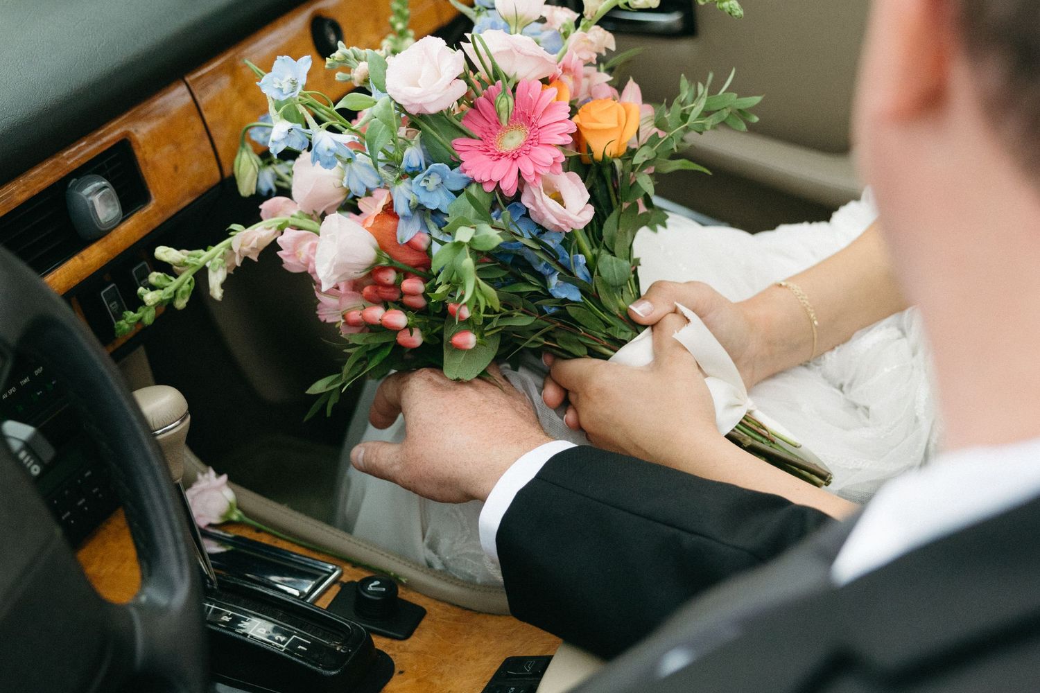 Wedding couple examining colorful floral bouquets in car interior.