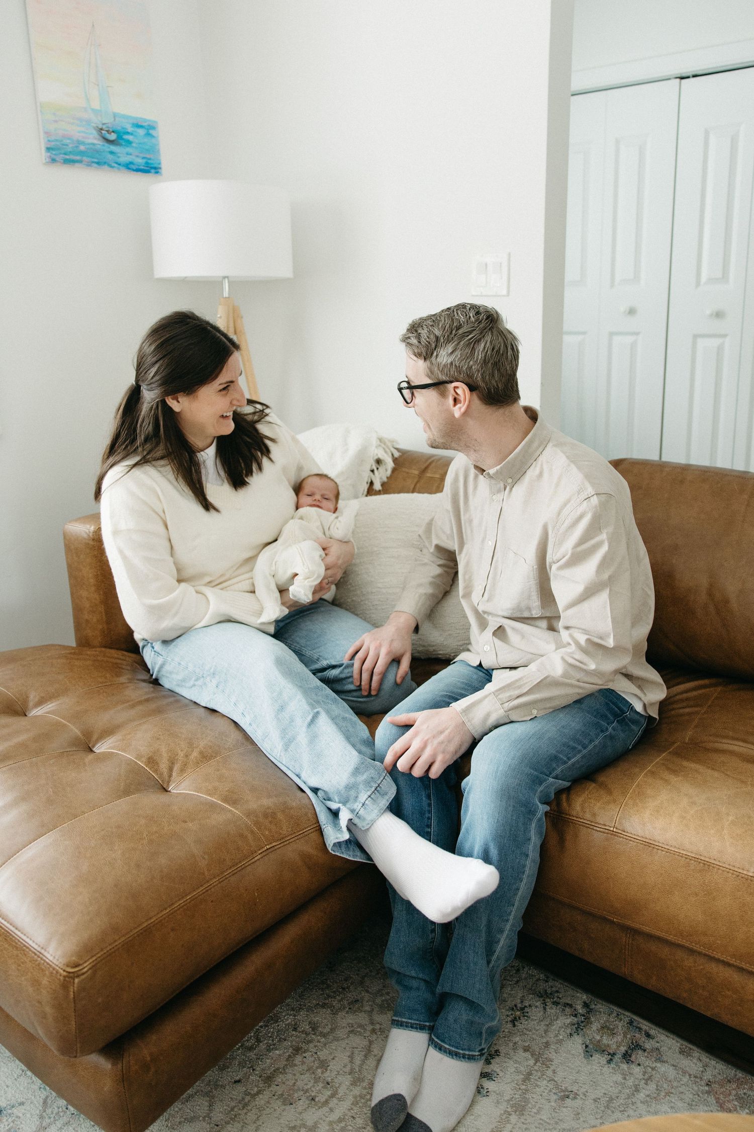 Couple sitting together on brown leather couch sharing intimate conversation in living room.