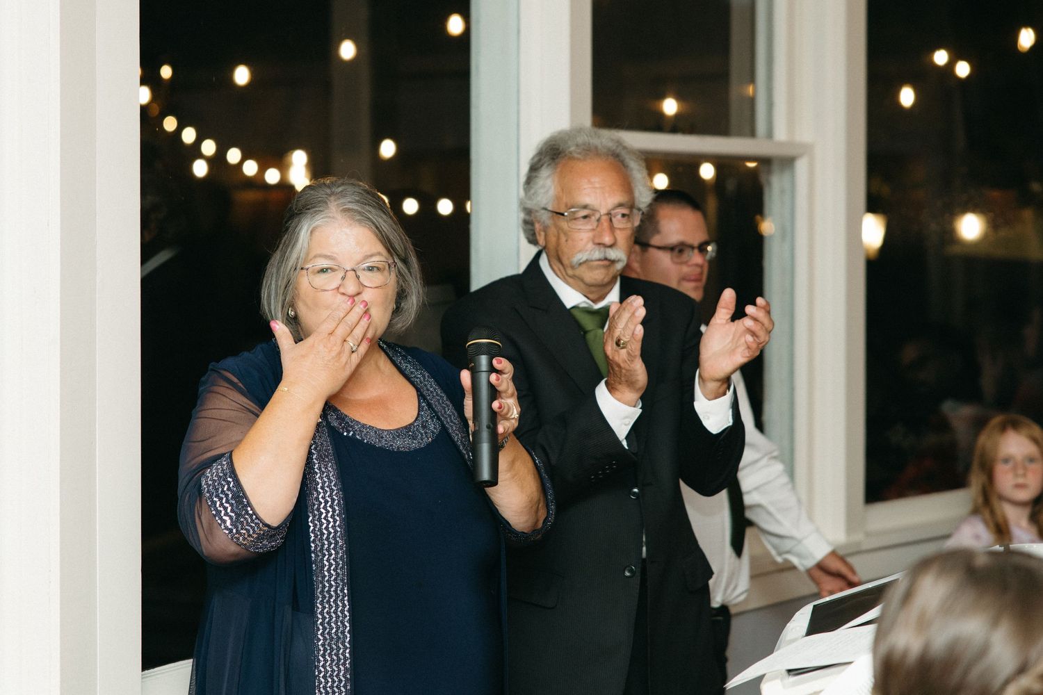 Older couple giving wedding toast speech with microphone at evening reception venue.