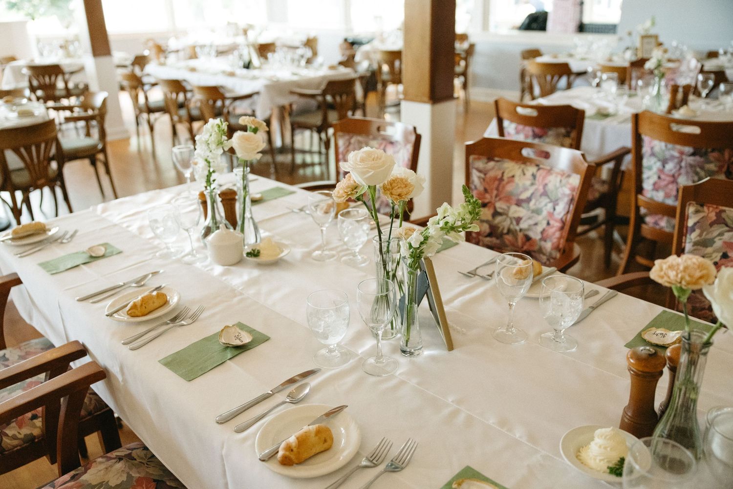 Elegant wedding reception tables set with white linens, green napkins, and delicate floral centerpieces.