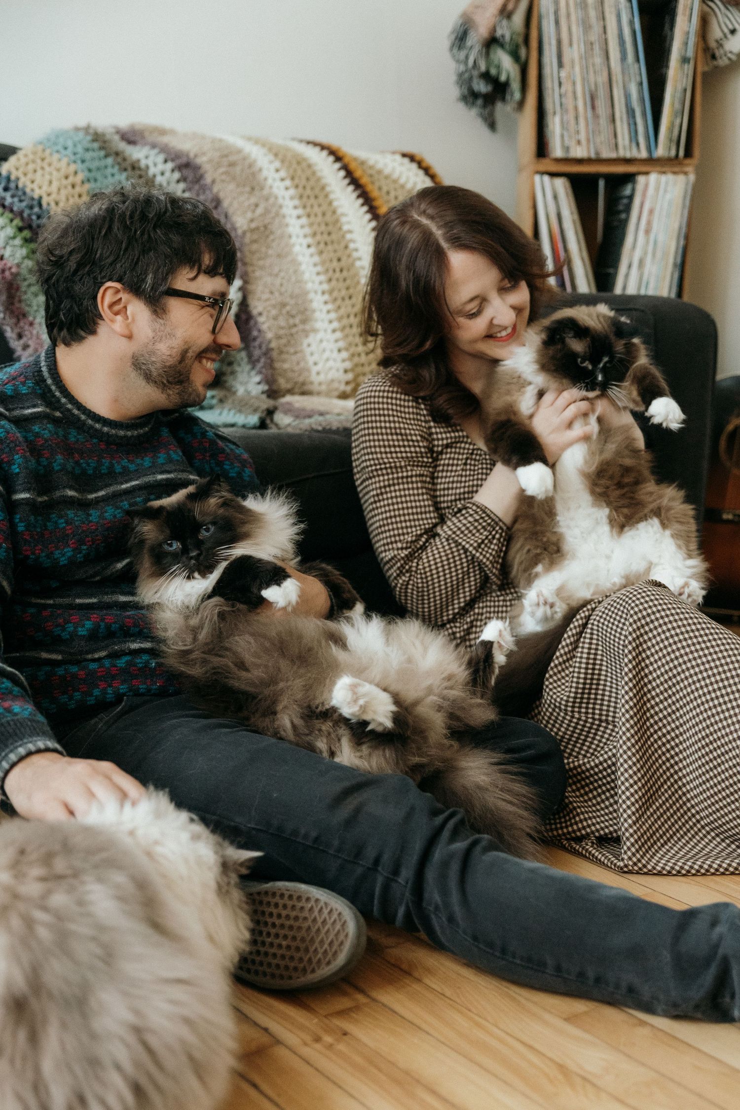 Couple sitting on floor with two fluffy Ragdoll cats in a cozy living room.