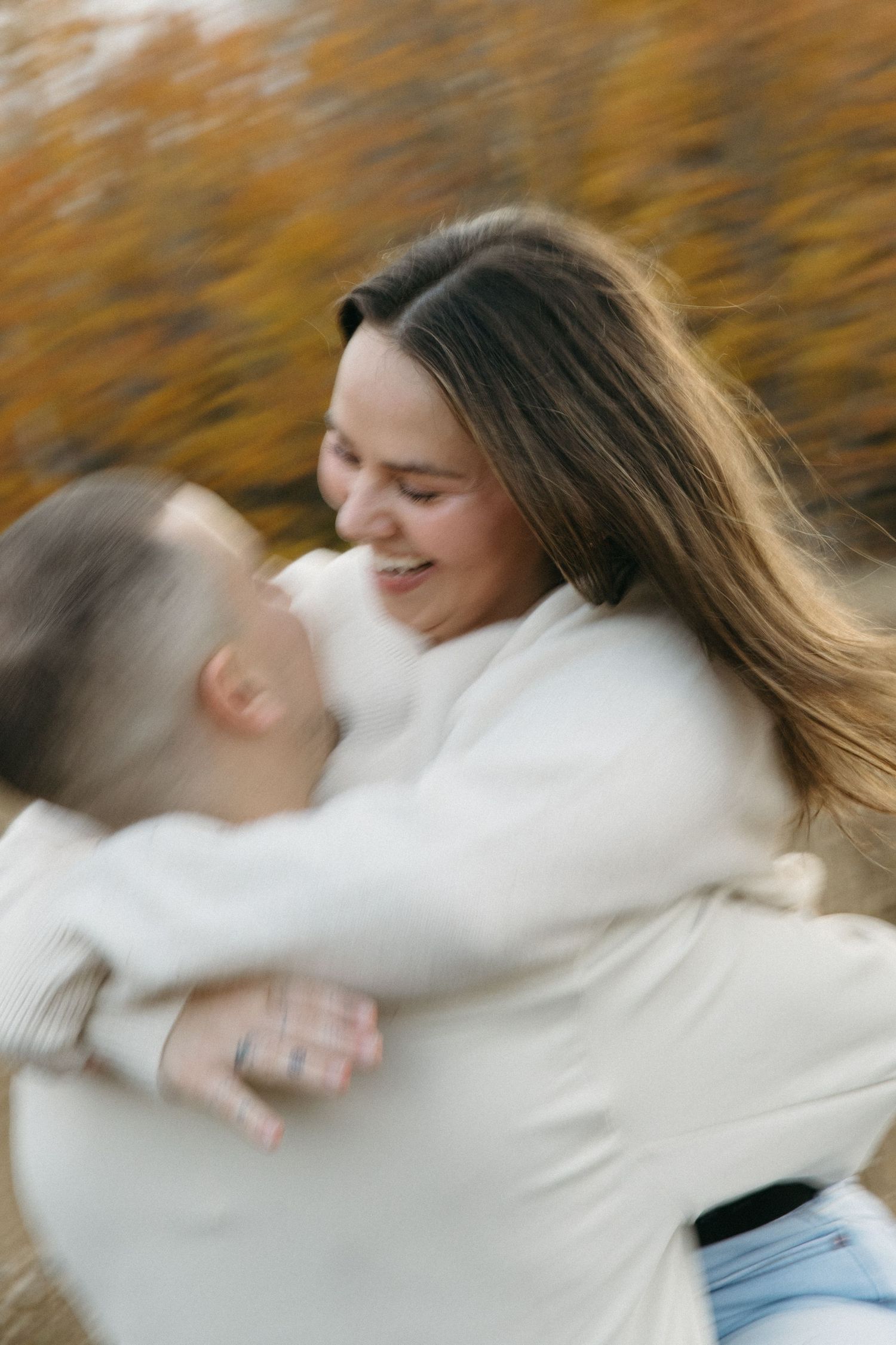 Couple spinning and dancing together in a field with autumn trees in the background.