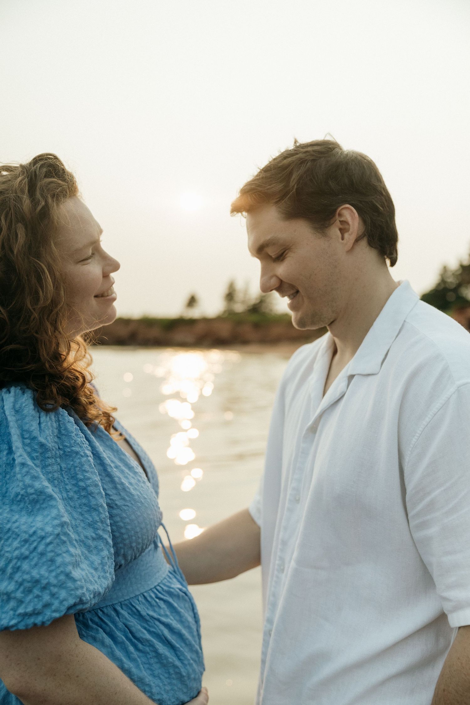 Couple sharing intimate moments on a beach at sunset with sparkling water in the background.