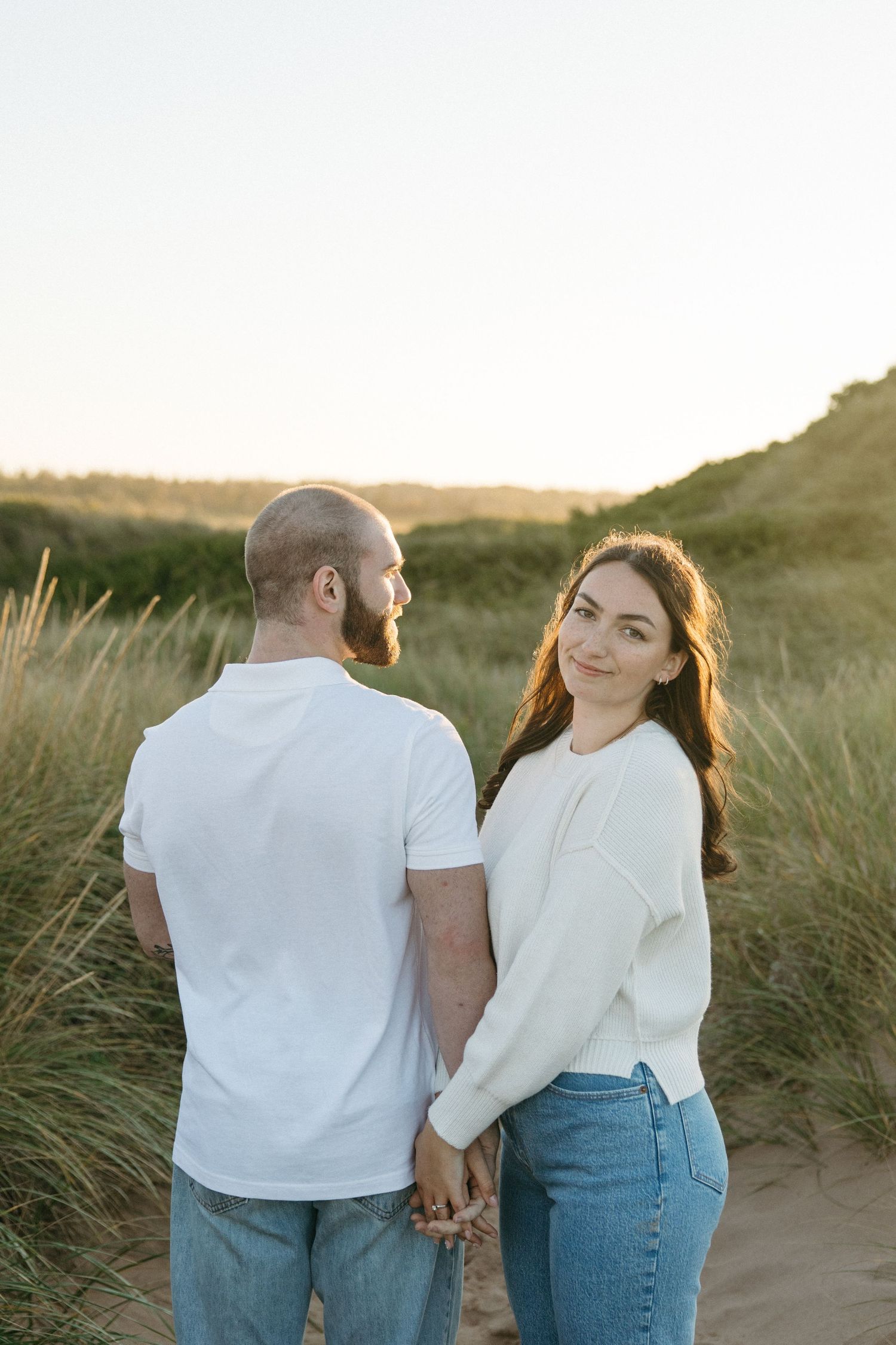 Couple in matching white tops and jeans sharing tender moment on beach.