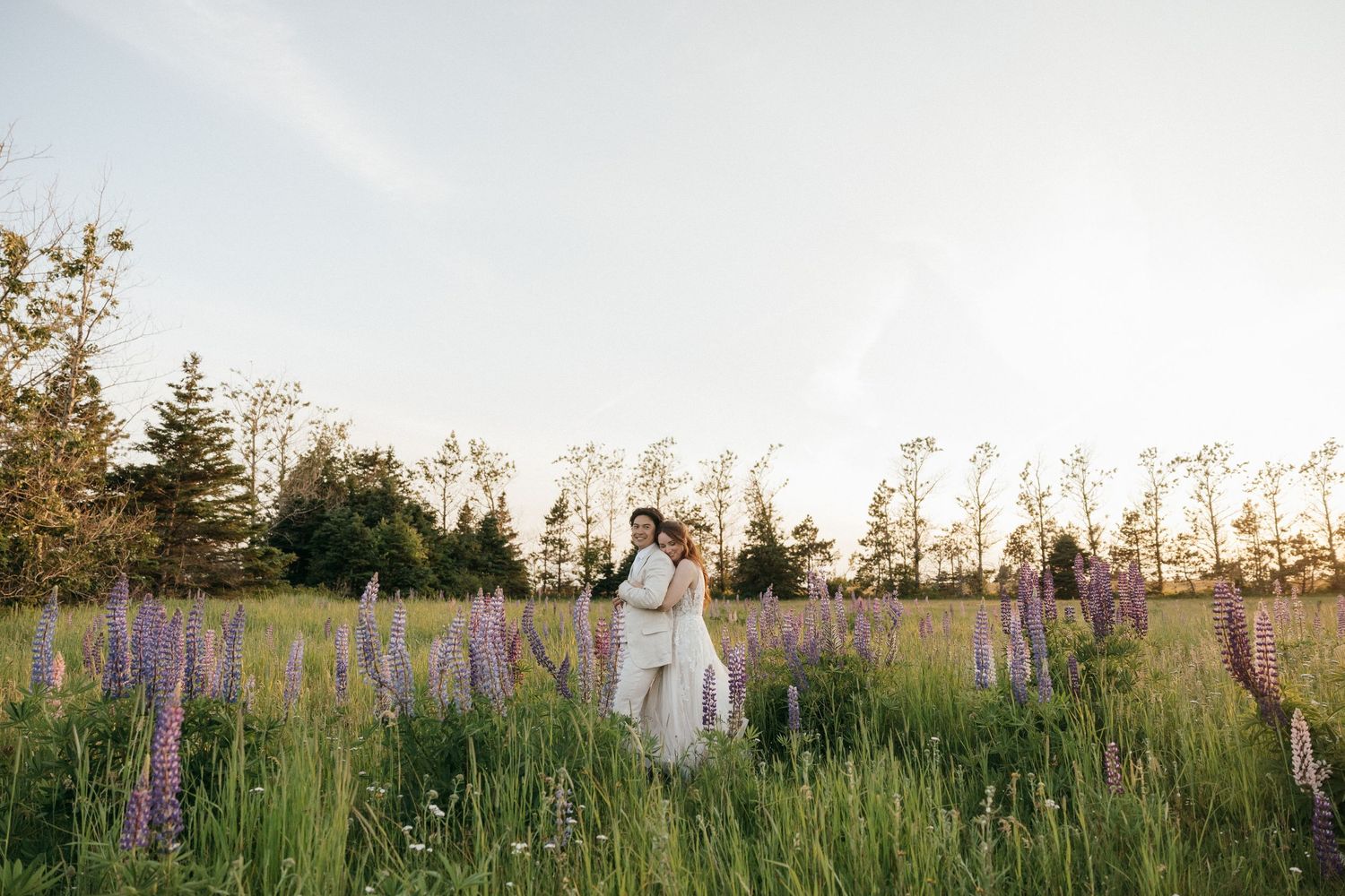Wedding couple poses in field of purple wildflowers during golden hour.