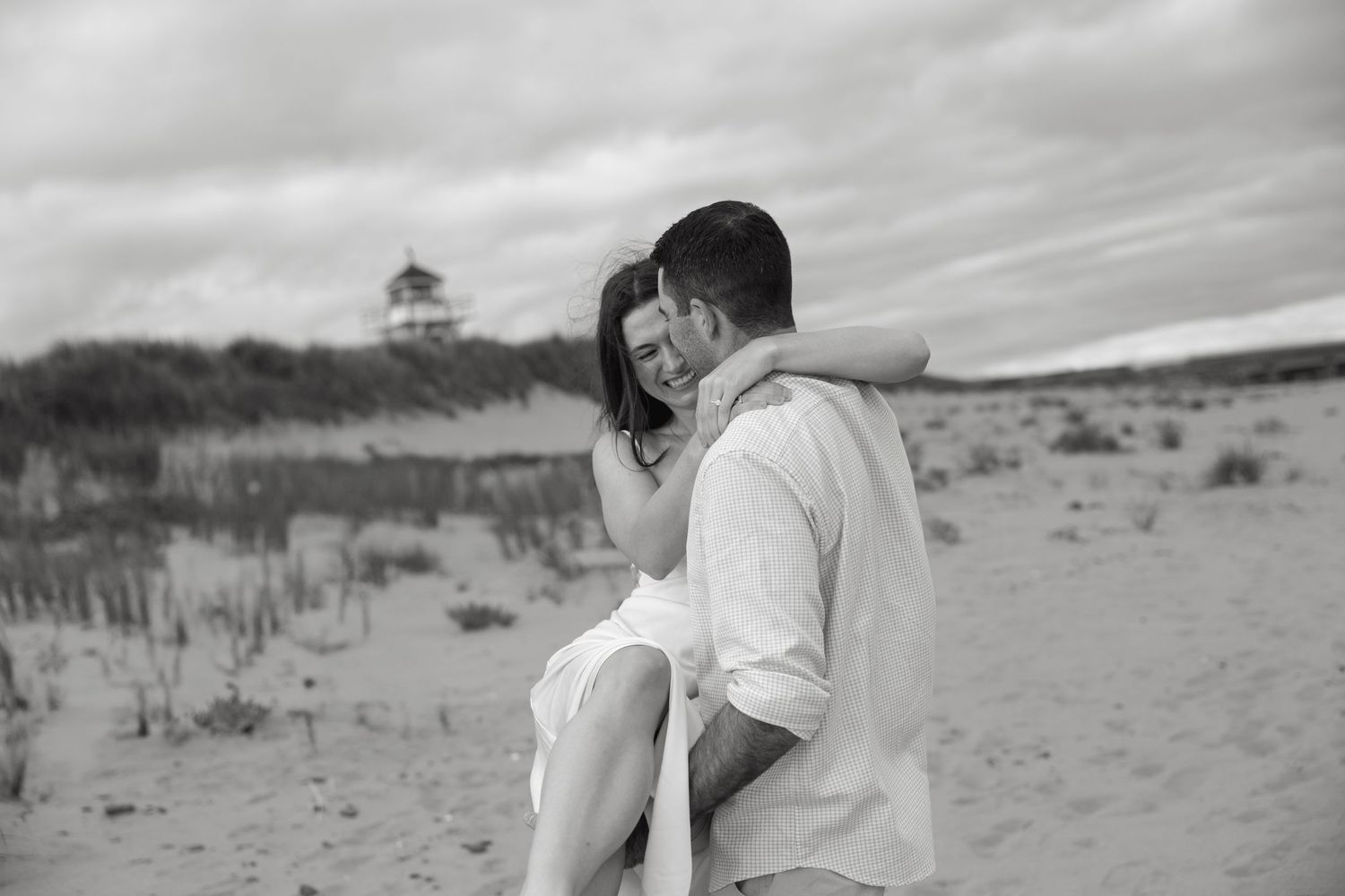 A black and white beach portrait of a couple sharing an intimate moment near sand dunes.