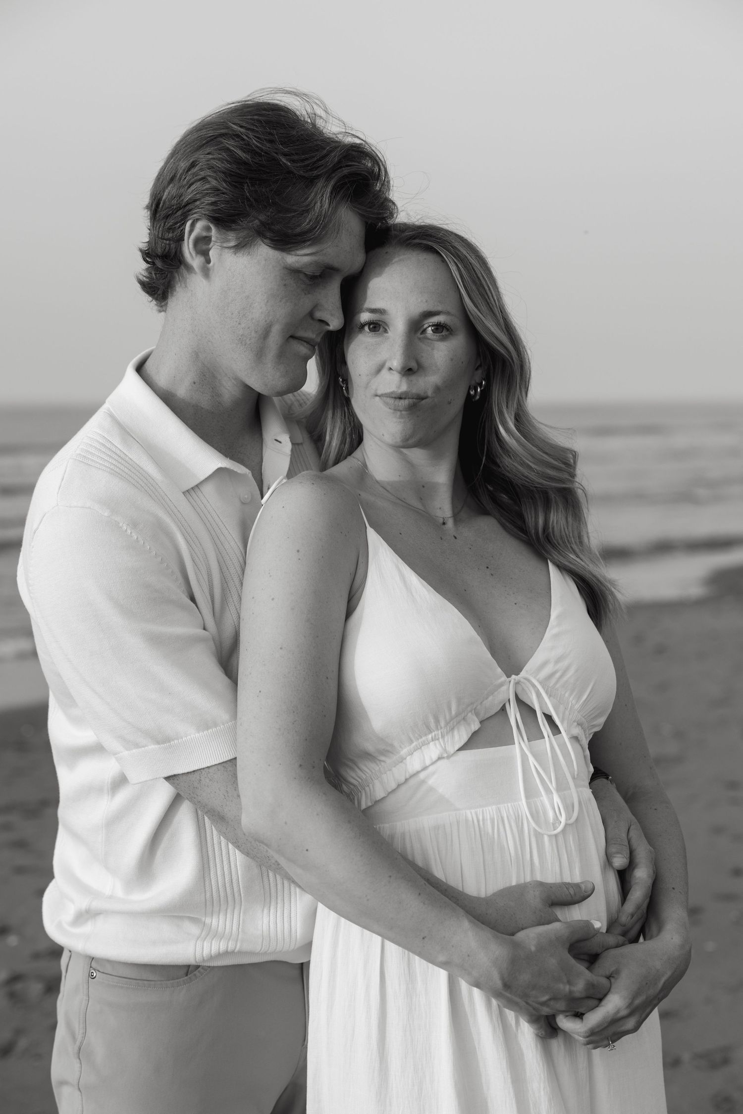 Black and white portrait of couple embracing on beach, man holding woman from behind tenderly.