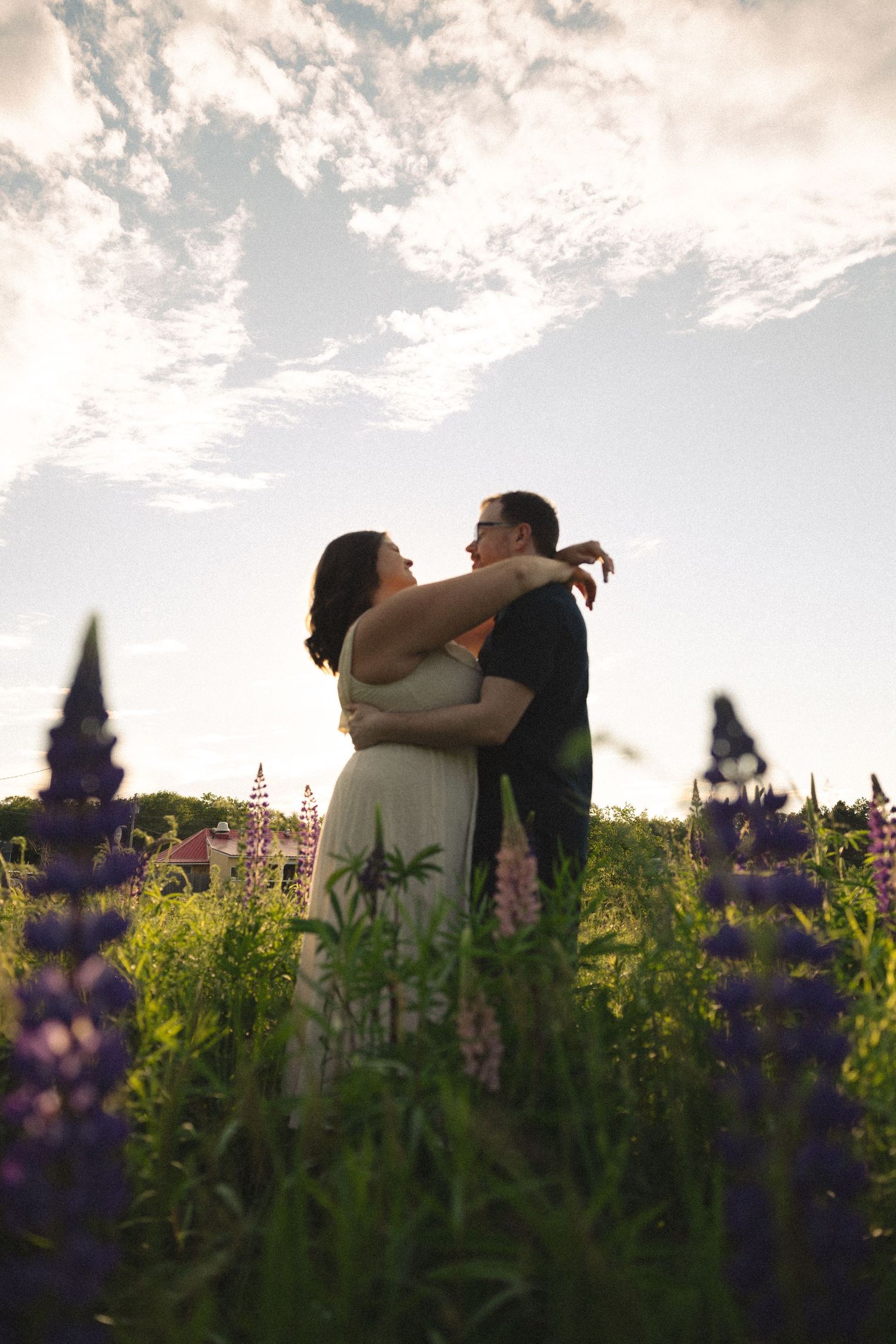 Romantic couple embracing in field of purple lupine flowers under dramatic cloudy sky.