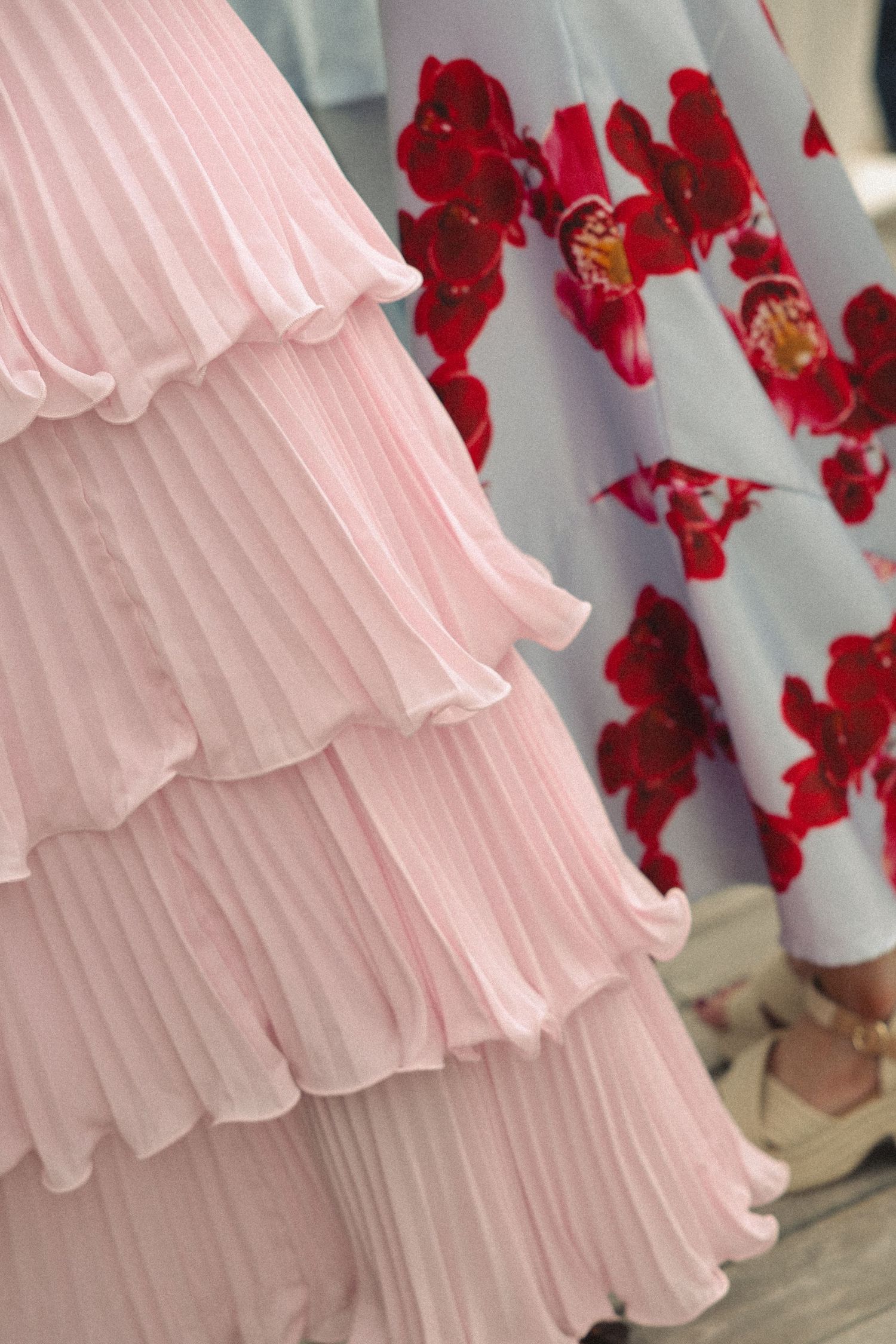 Elegant tiered pink pleated skirt beside a floral red and white dress, showcasing fashion design details.