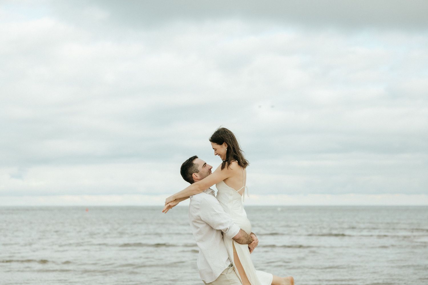Two people in white outfits dancing and playing together by the ocean.