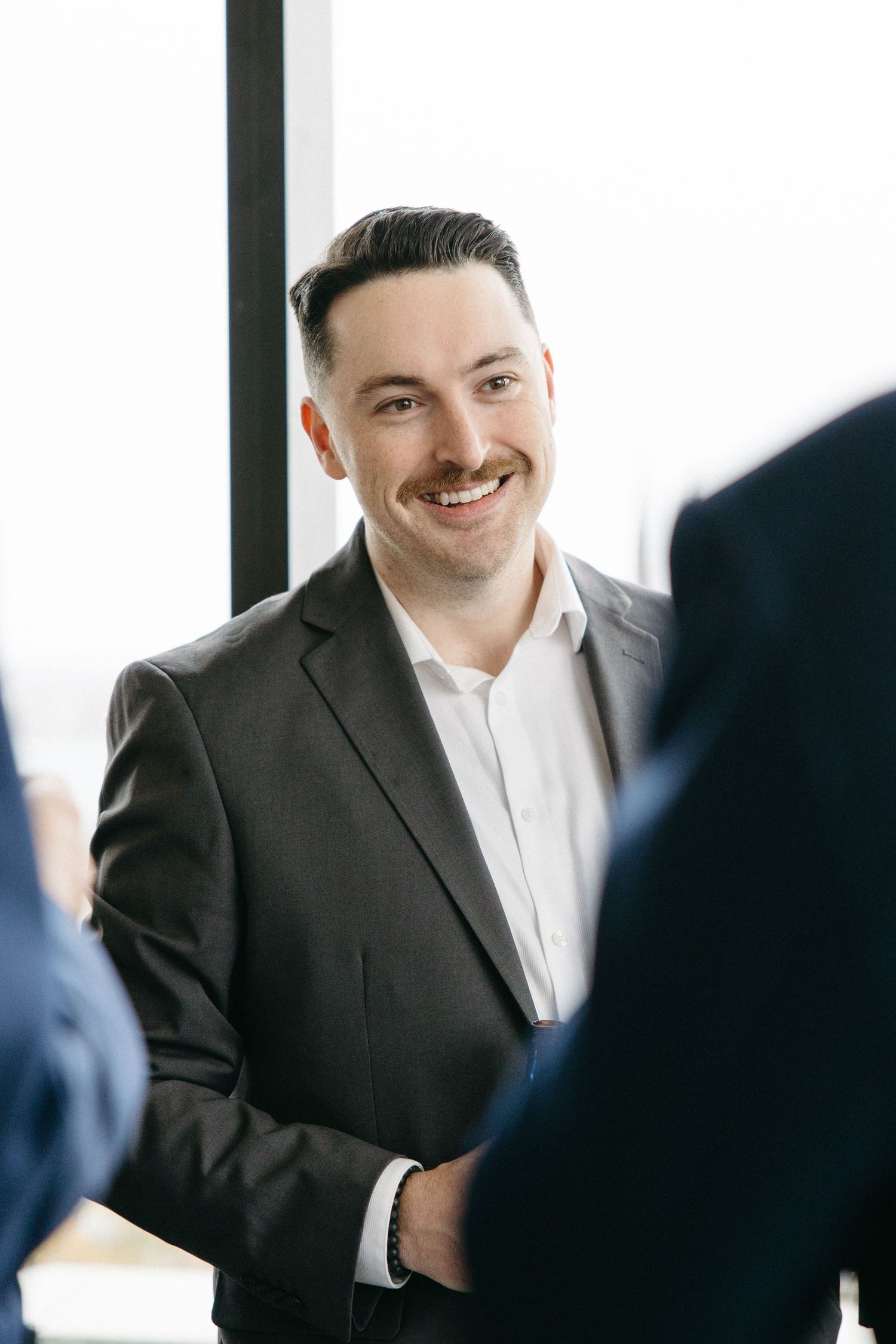 A person in a dark suit smiles warmly in front of a bright white background.