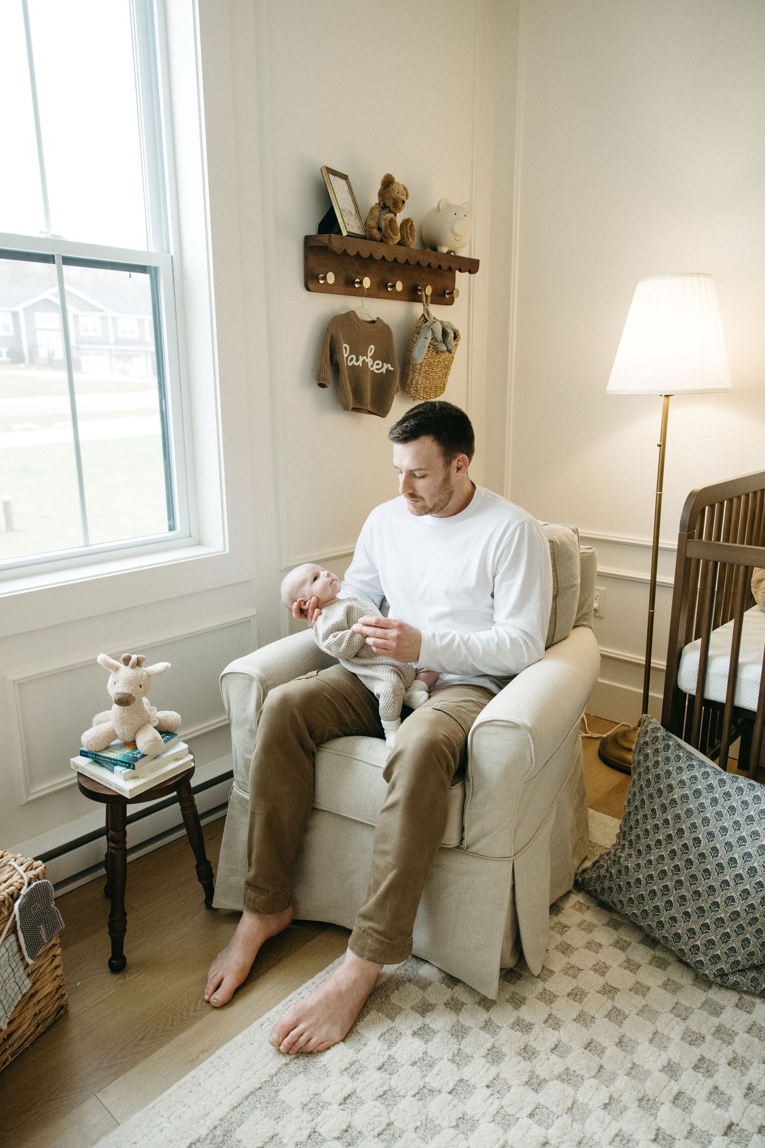 A tranquil nursery scene with a white armchair, wooden crib, and wall-mounted shelving displaying baby items.