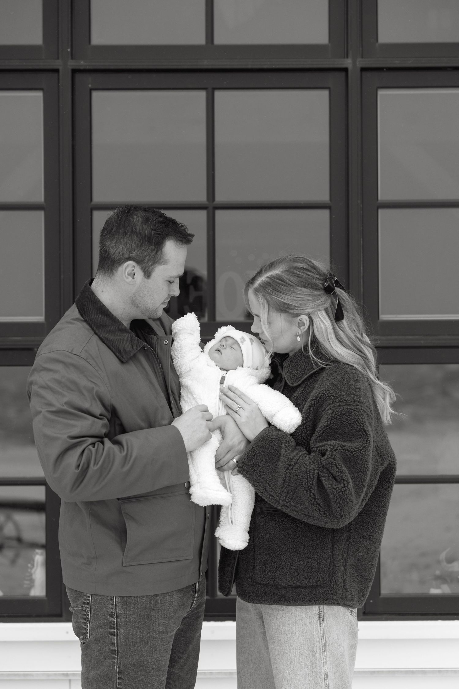 A couple shares an intimate moment with their newborn baby in front of a window.