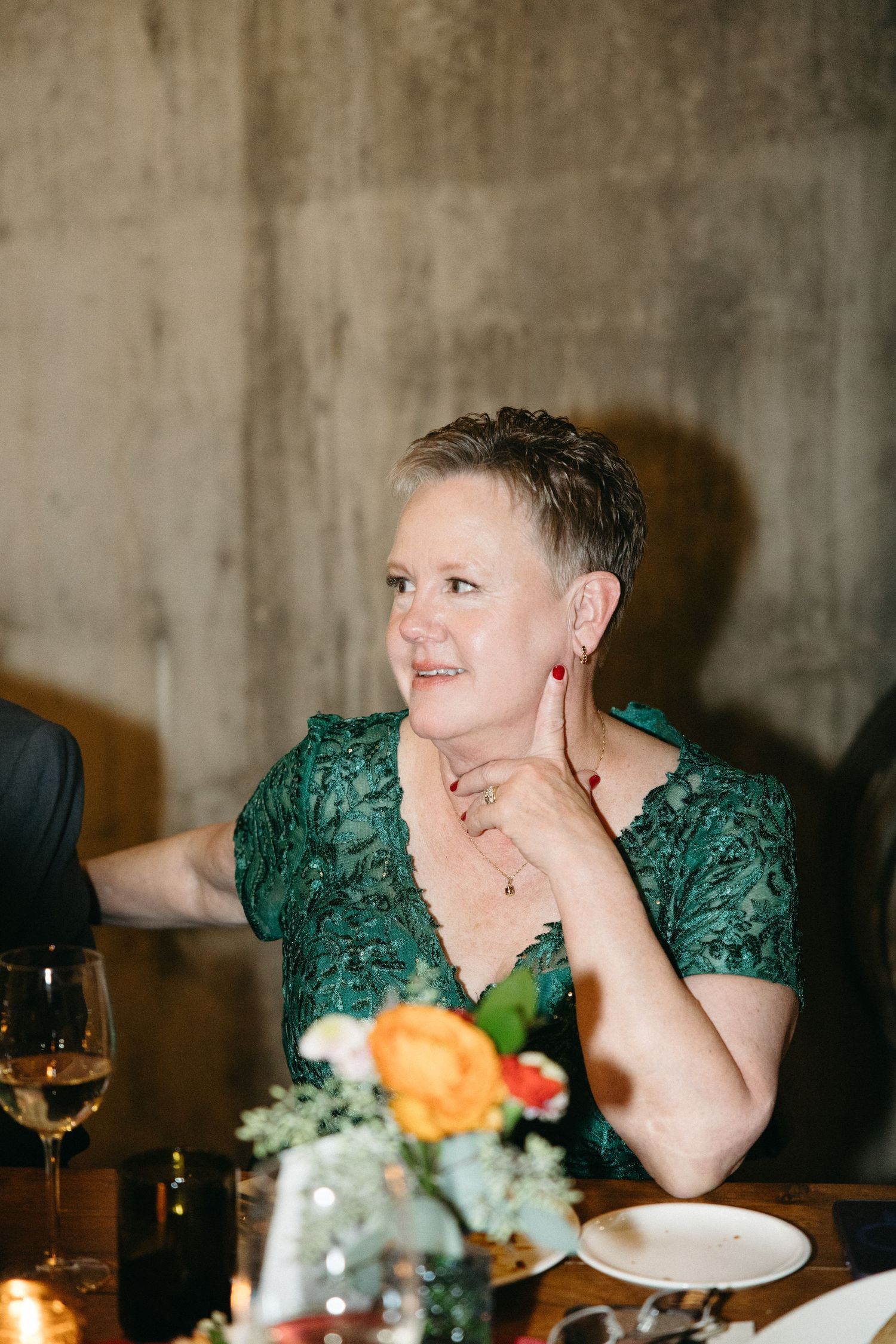 Guest in emerald lace dress seated at elegant wine cellar dinner party.