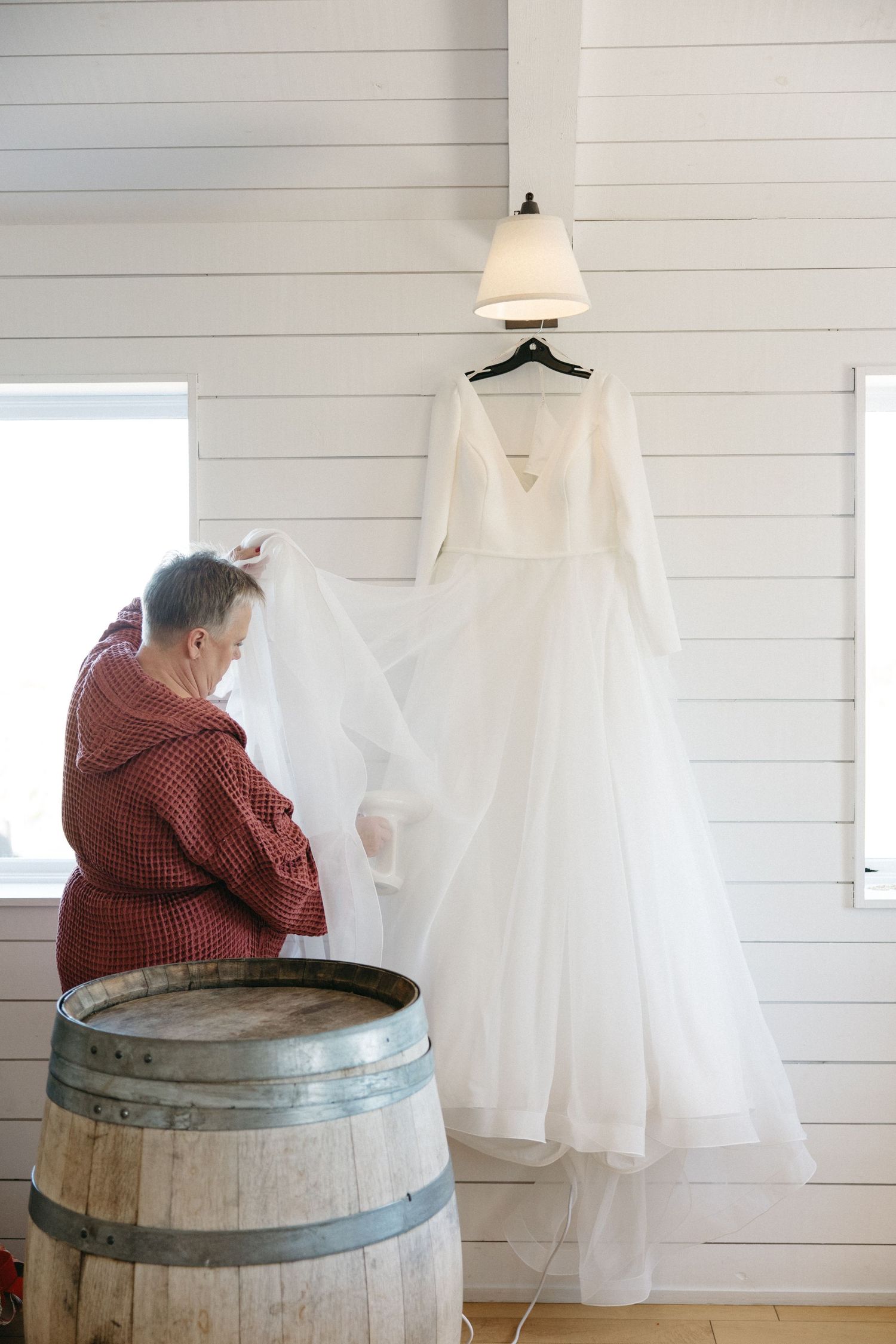 White wedding dresses displayed next to rustic wine barrels in a bright room.