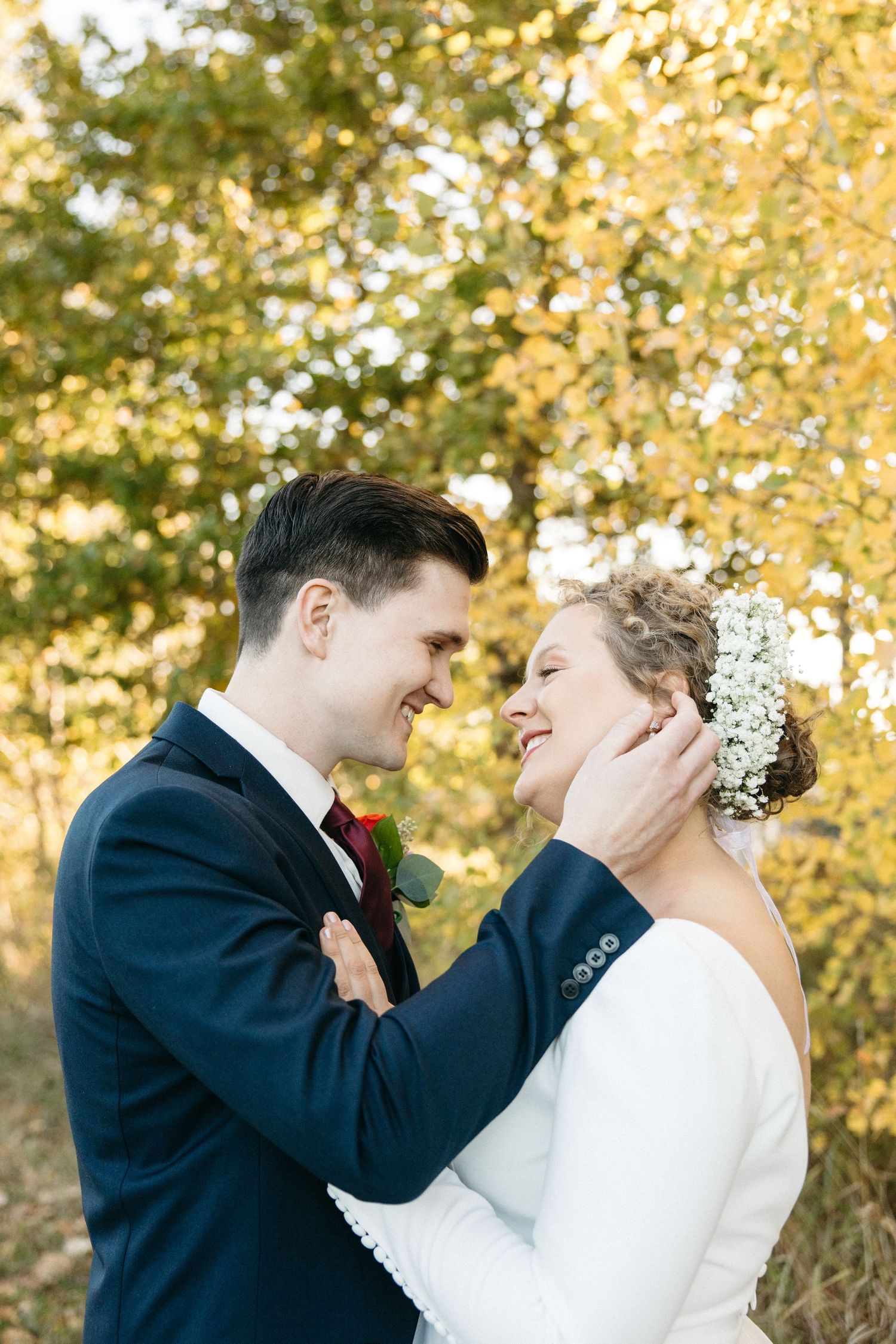 A romantic wedding couple embraces in front of golden autumn foliage during their outdoor photo session.