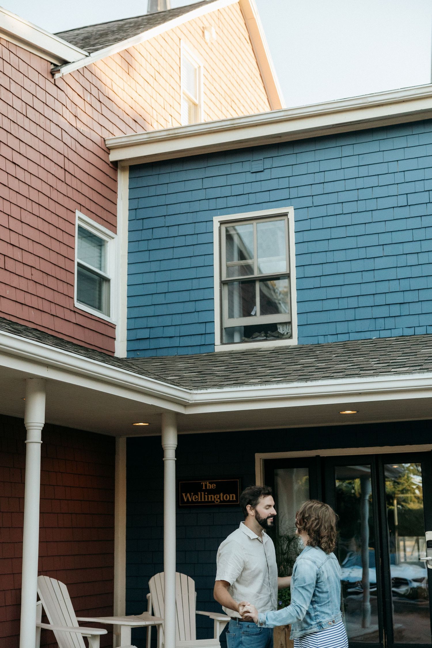 Two people stand together outside a blue and red shingled building entrance.