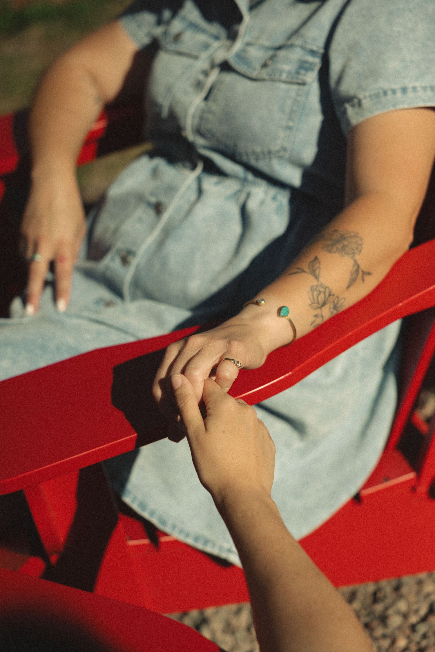 Close-up of denim clothing and hands resting on a bright red outdoor chair.