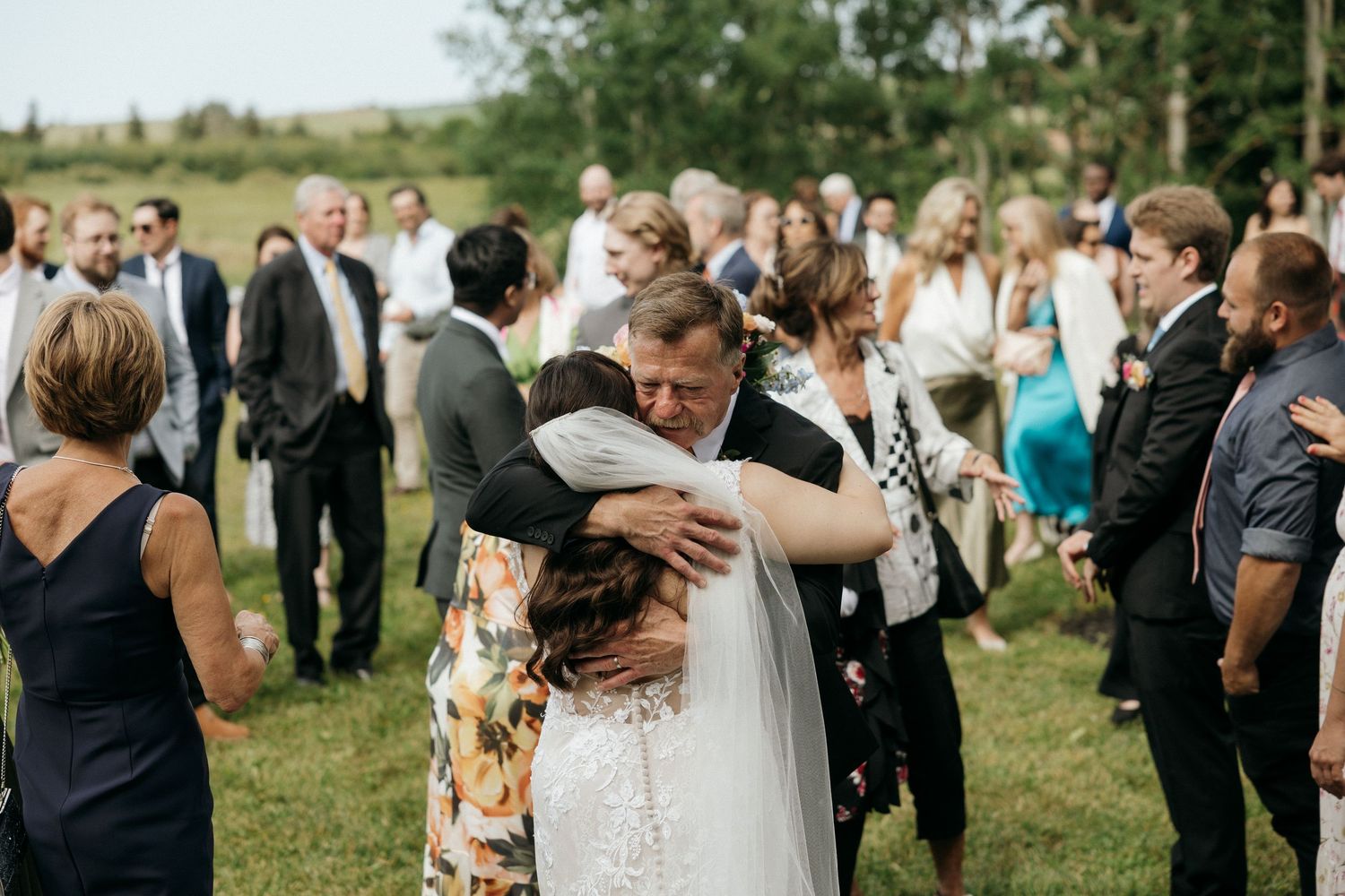 Wedding guests mingle and embrace during an outdoor garden reception.