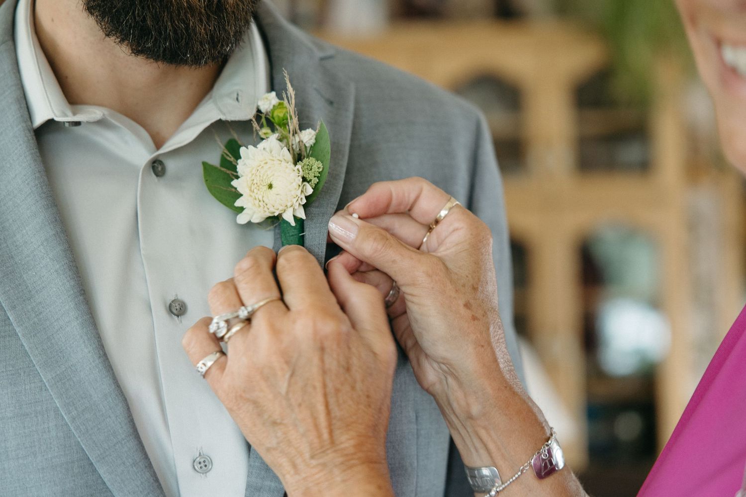 Close-up of hands pinning a white floral boutonniere onto a light gray suit jacket.