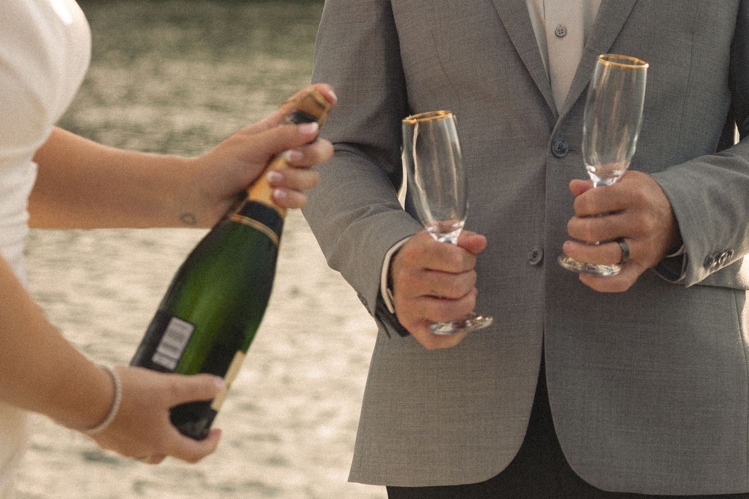People in formal attire hold champagne glasses and bottles during an outdoor celebration.