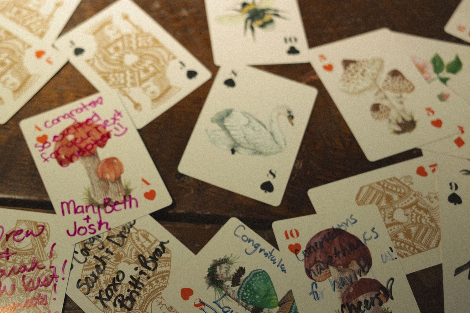 Playing cards spread out on a wooden surface with handwritten messages and decorative designs.