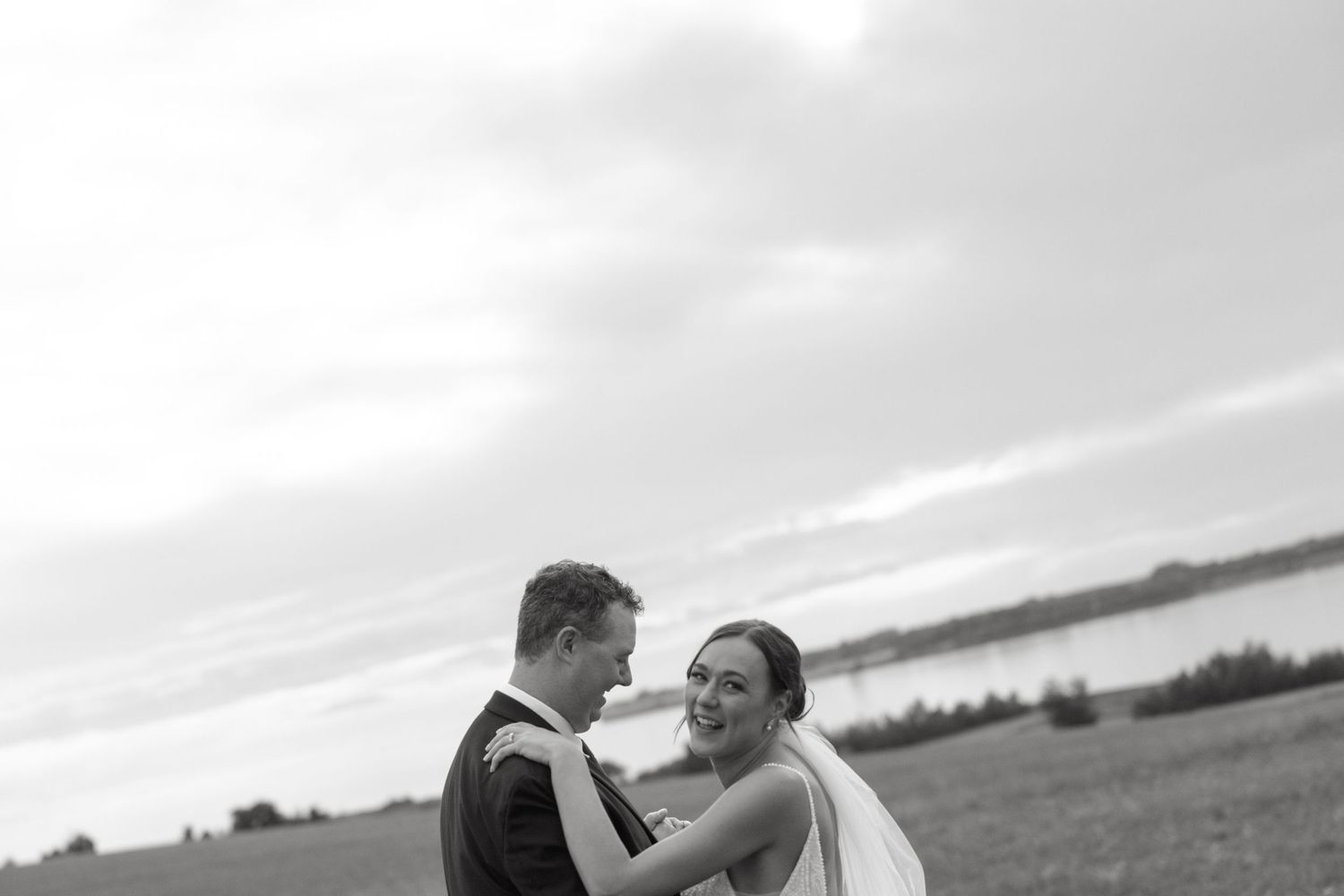 Couple embracing during outdoor wedding photoshoot with cloudy sky background.