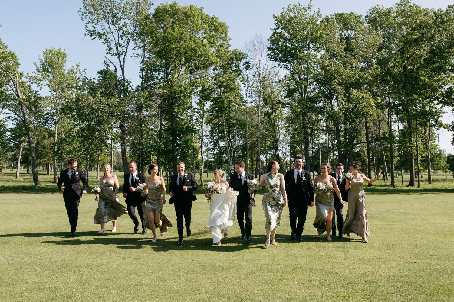 Bridal party and groomsmen posing for formal photos in a park setting.
