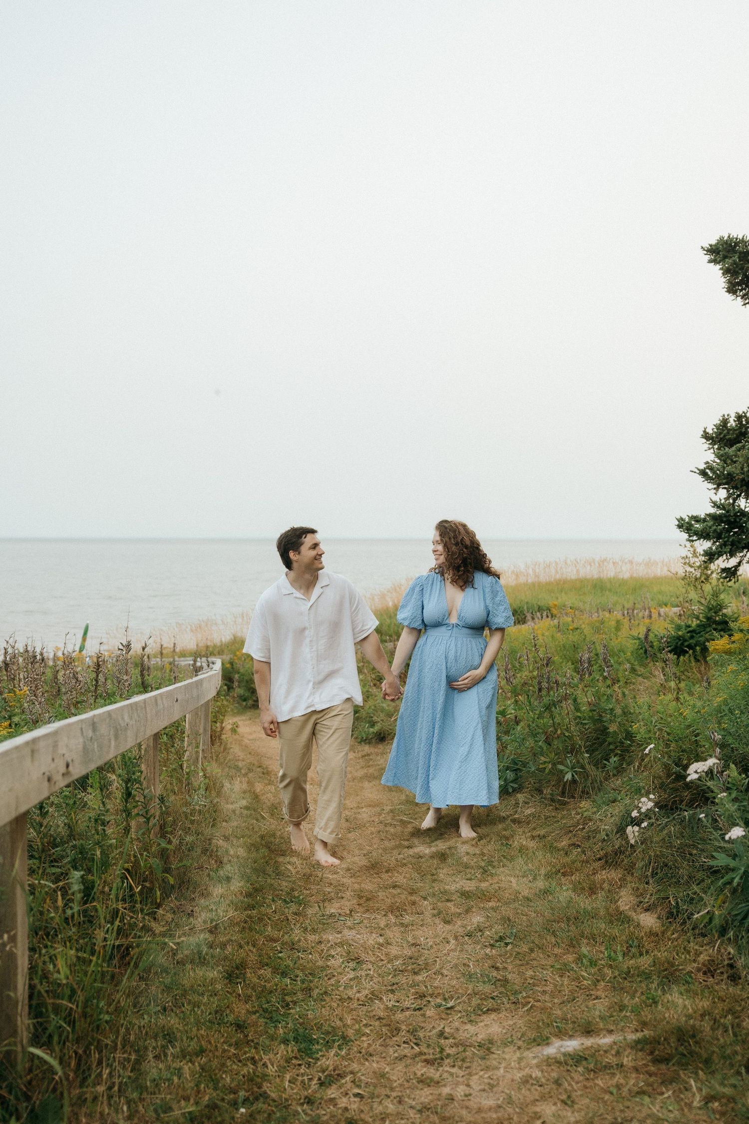 A couple walks along a scenic coastal path surrounded by wildflowers and grass.
