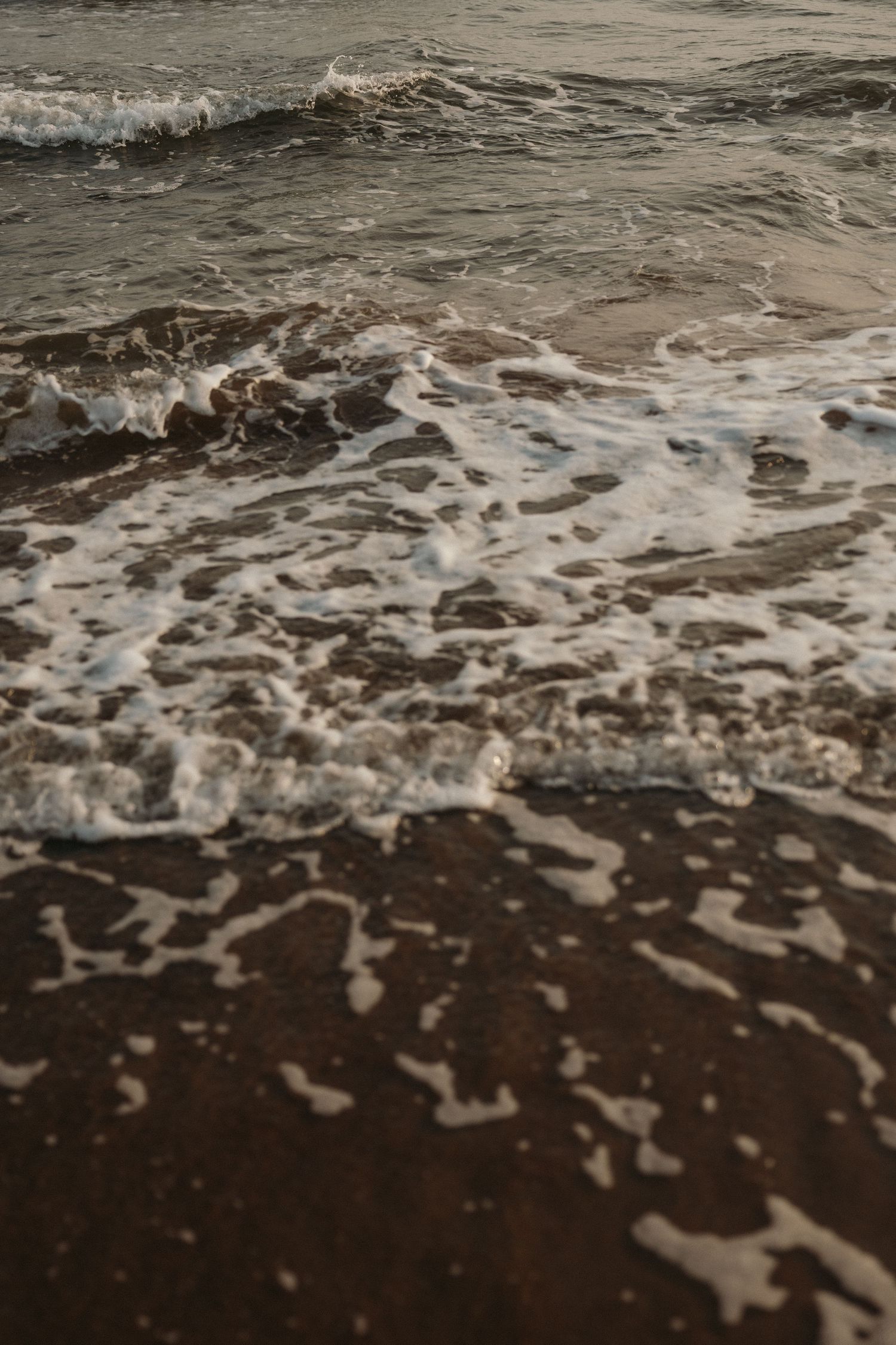 Ocean waves washing up on dark sandy beach creating white foam patterns.