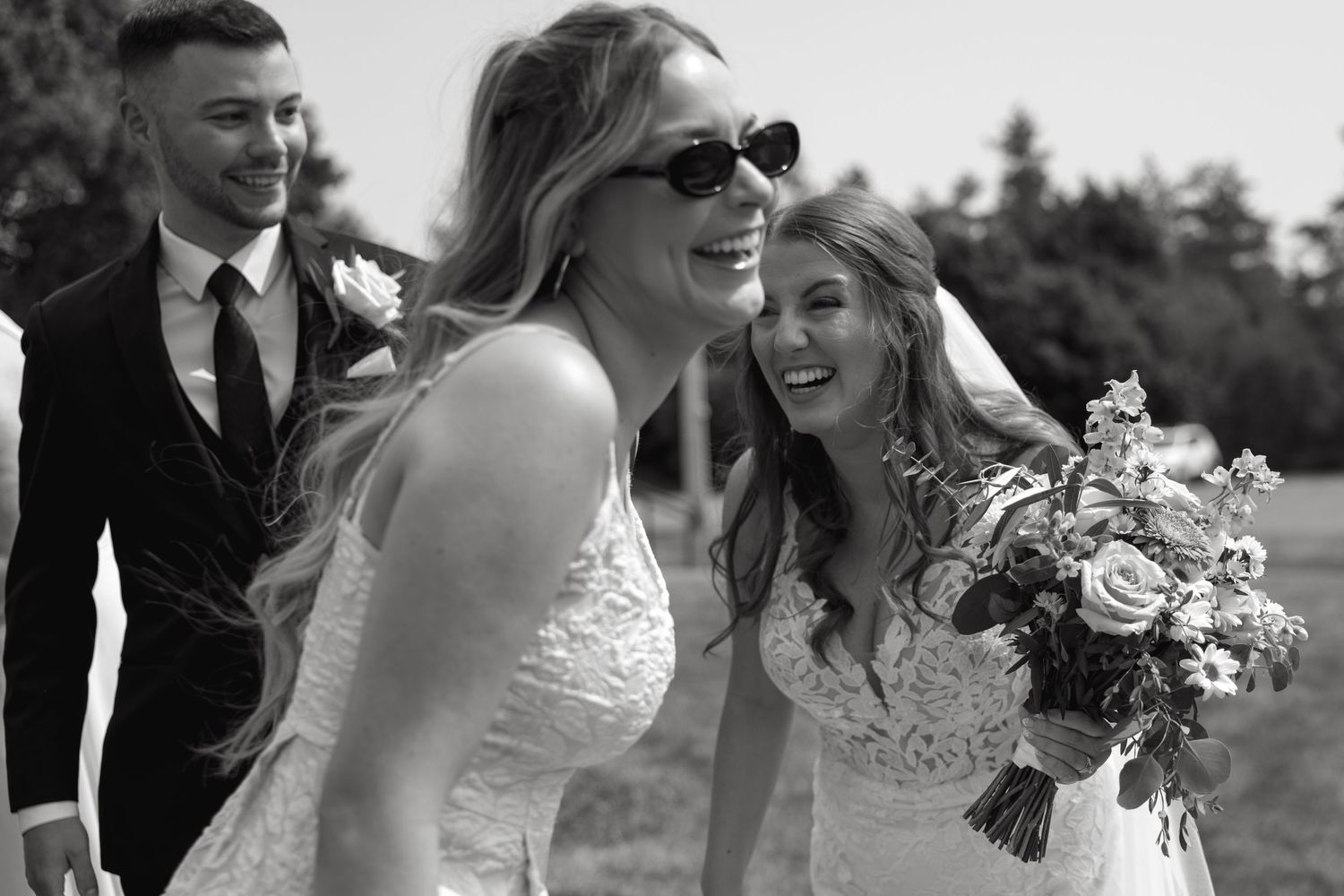 Black and white photo of wedding party enjoying candid moments outdoors.