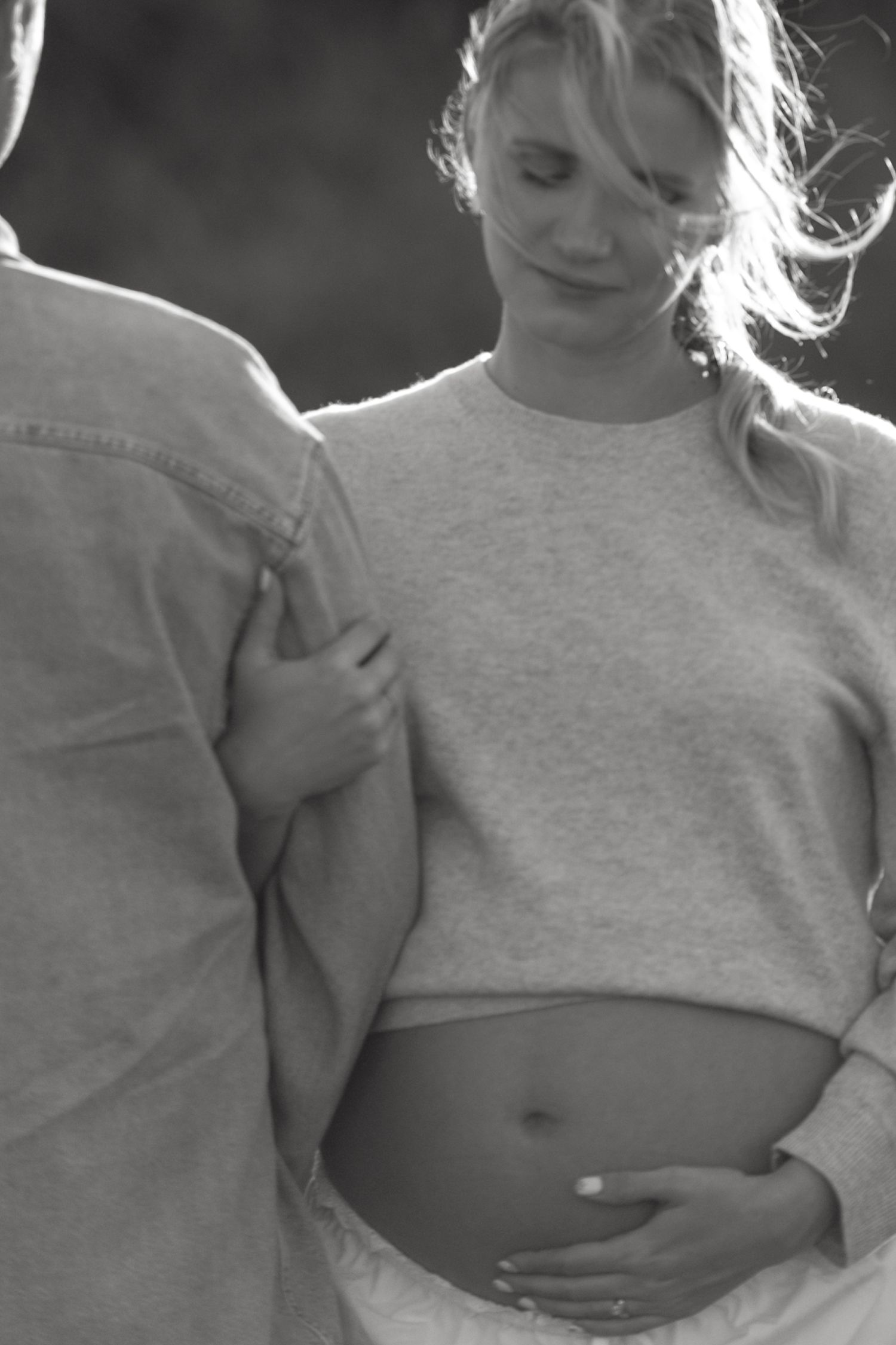 Black and white photo of an expectant mother in a cropped sweater cradling her pregnant belly.