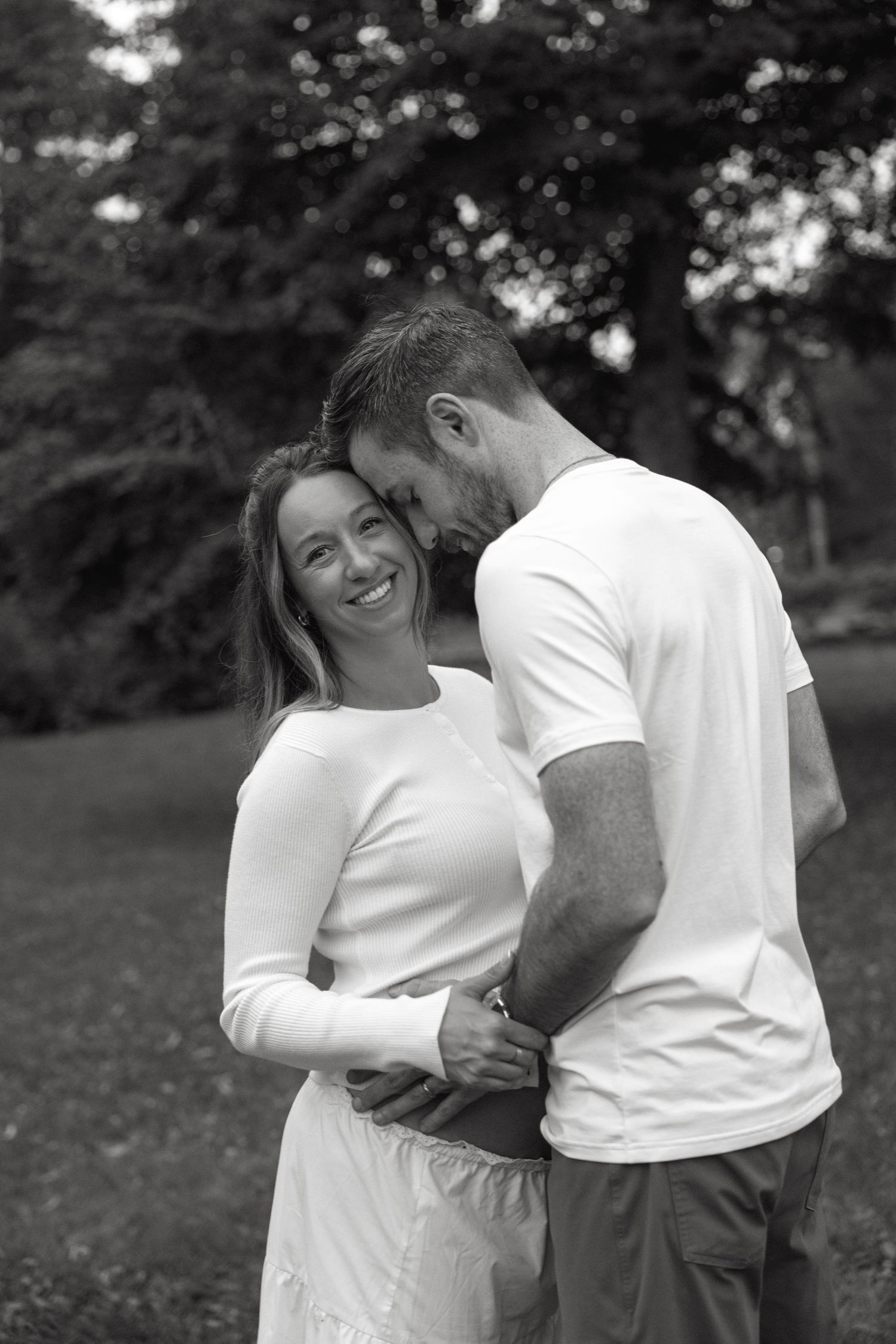 Black and white photo of a smiling couple embracing tenderly in a lush outdoor garden setting.