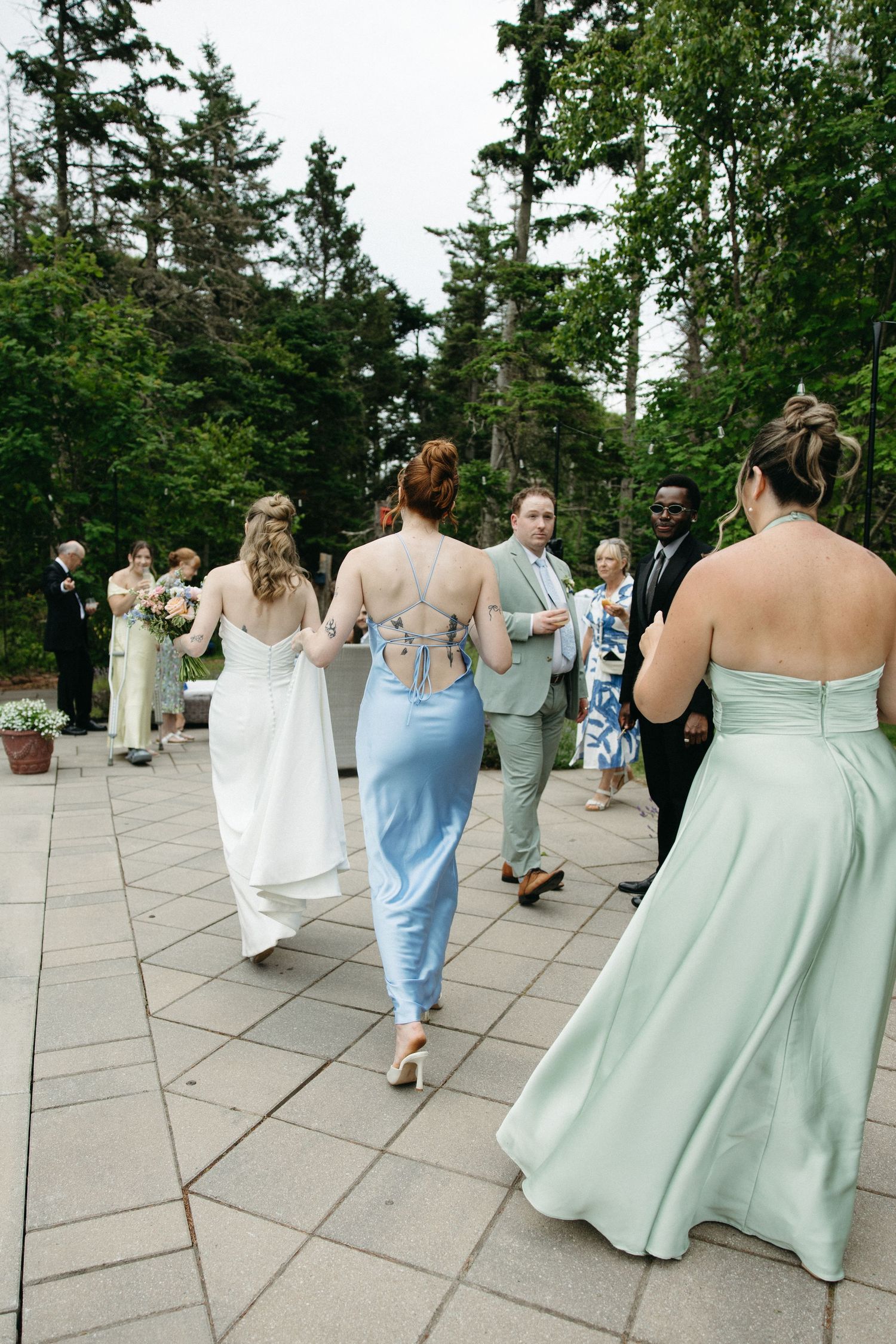 Bridesmaids in blue and mint gowns walk with bride on stone patio at outdoor wedding.