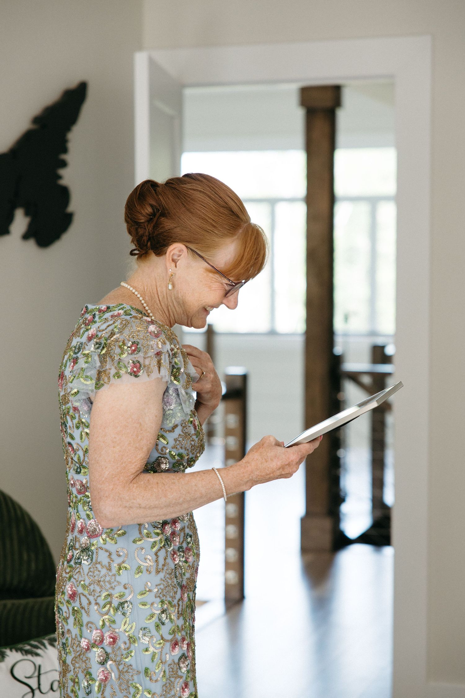 Elegant older woman in floral dress reading a card and smiling during a wedding celebration indoors.