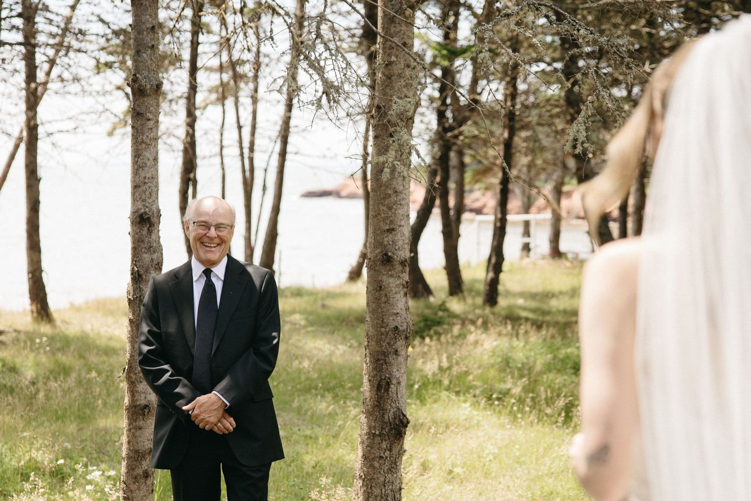 Emotional father sees bride daughter for the first time on wedding day among trees near waterfront.