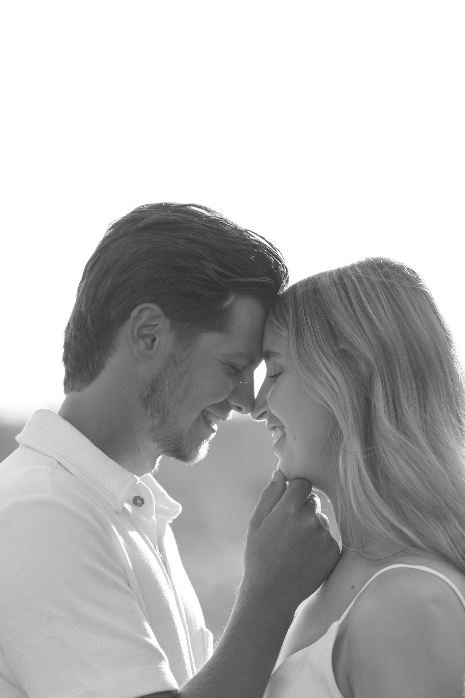 Black and white romantic portrait of a smiling couple touching foreheads in a tender moment.