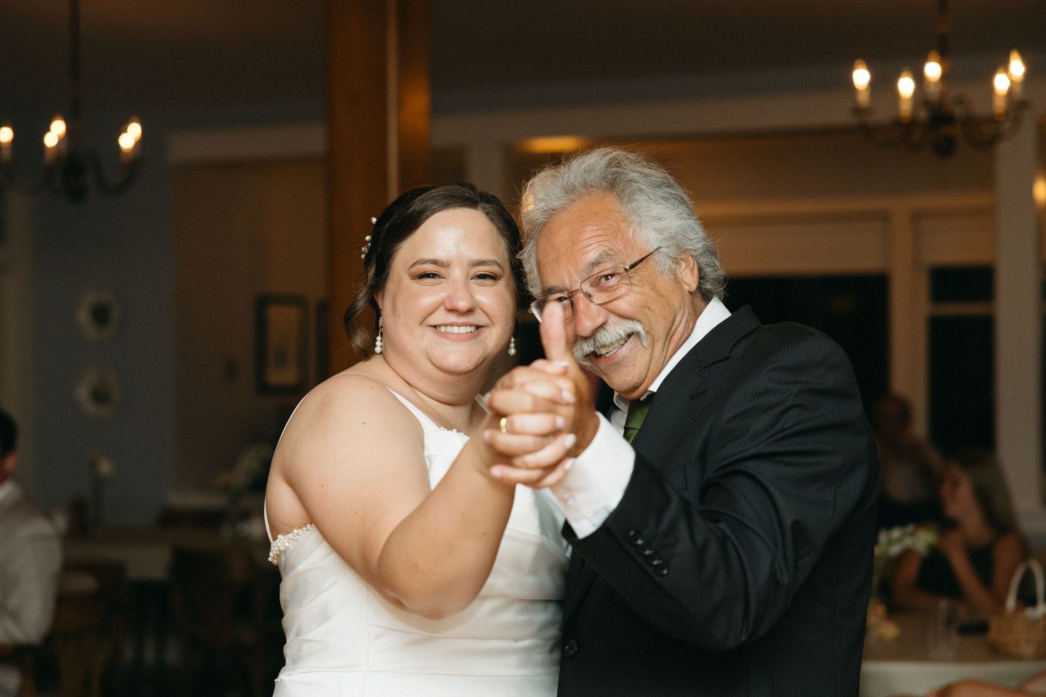 Bride and her father smile and dance together during wedding reception celebration.