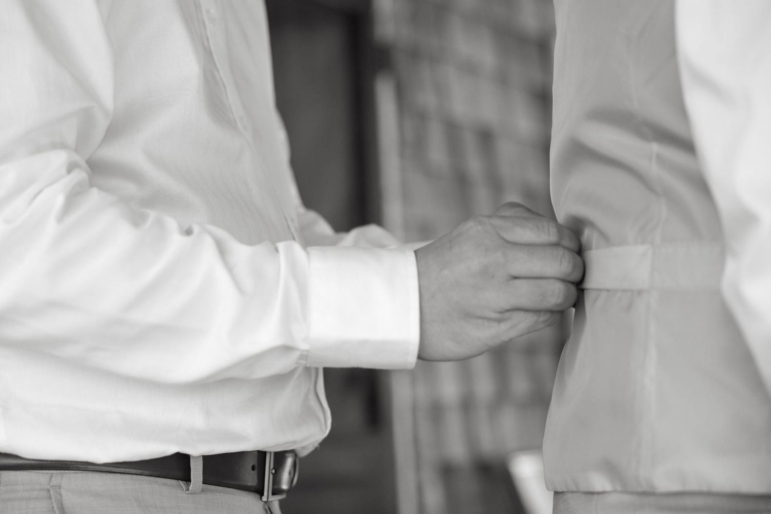 Black and white close-up of a groomsman adjusting the jacket of the groom before the wedding ceremony.
