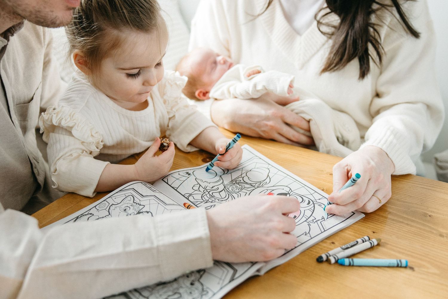 Family members coloring and drawing together at a wooden table with crayons and paper.