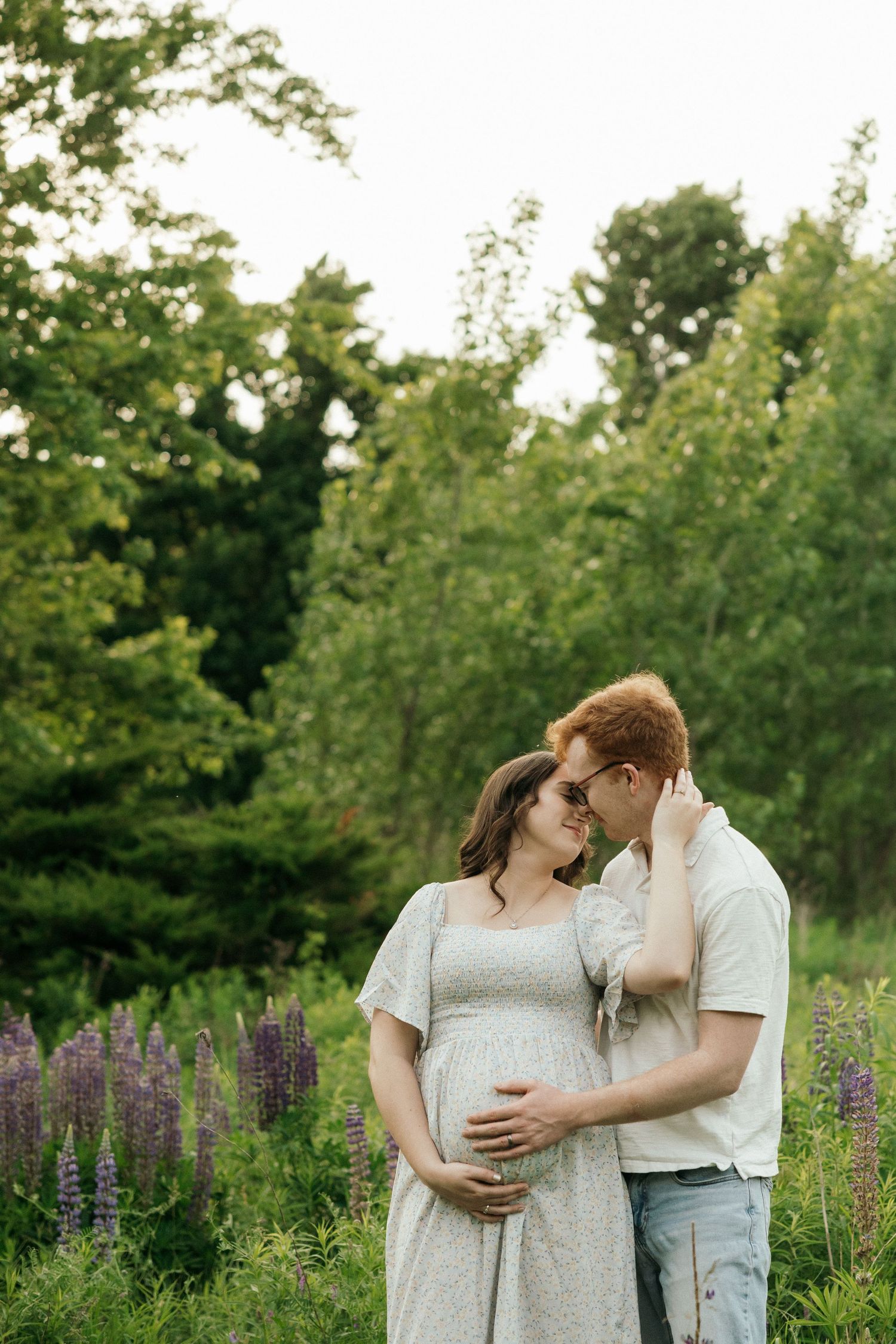 A couple embraces in a field of purple lupines and wildflowers during golden hour.