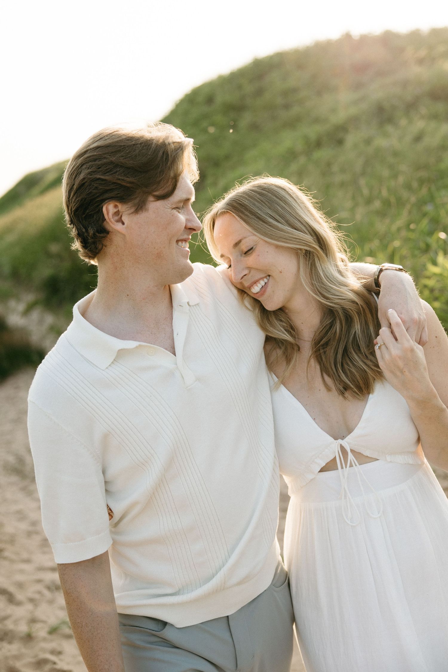 Happy couple smiling at each other while walking on sandy beach path at golden hour.