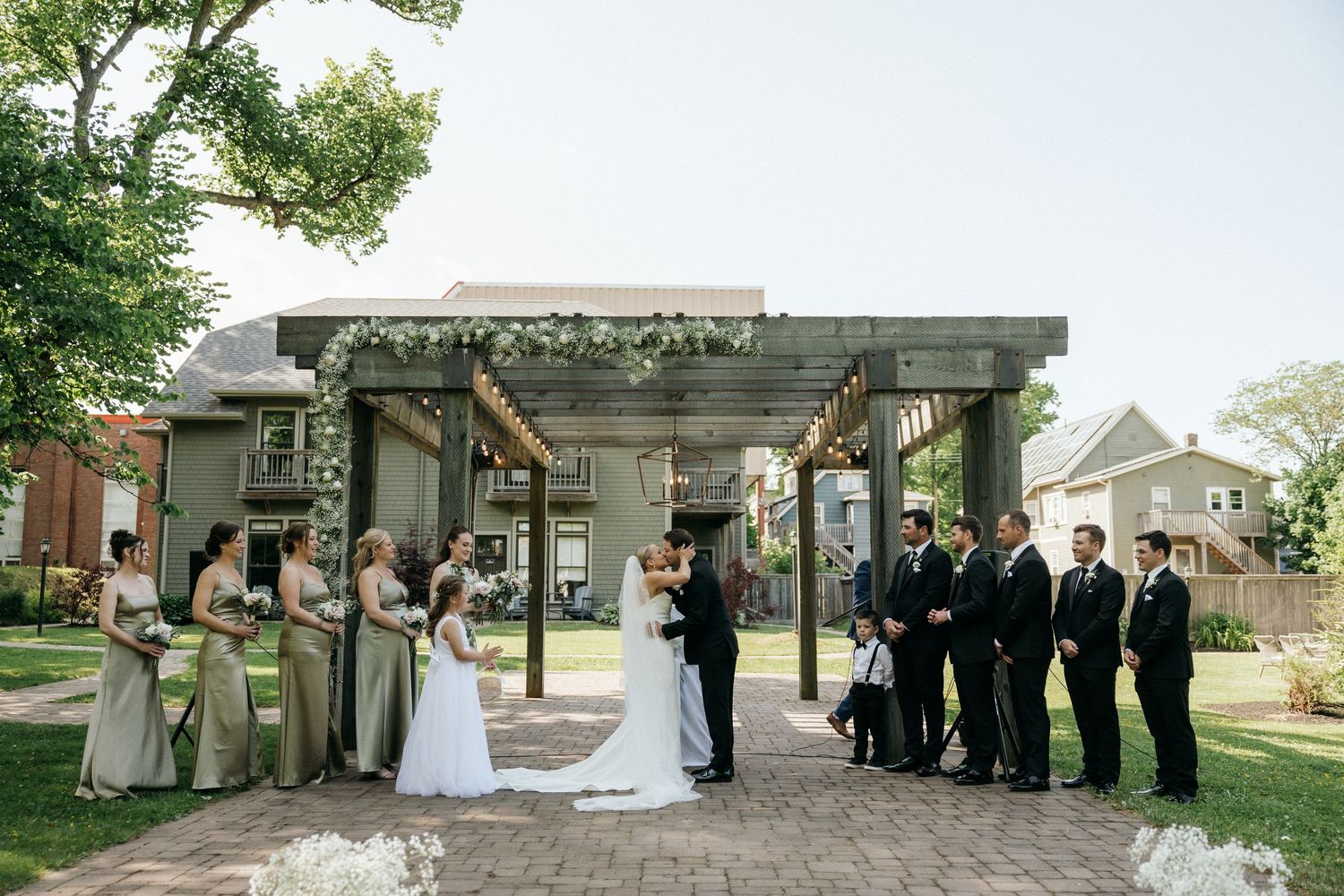 Wedding ceremony setup under a rustic wooden pergola with standing wedding party.