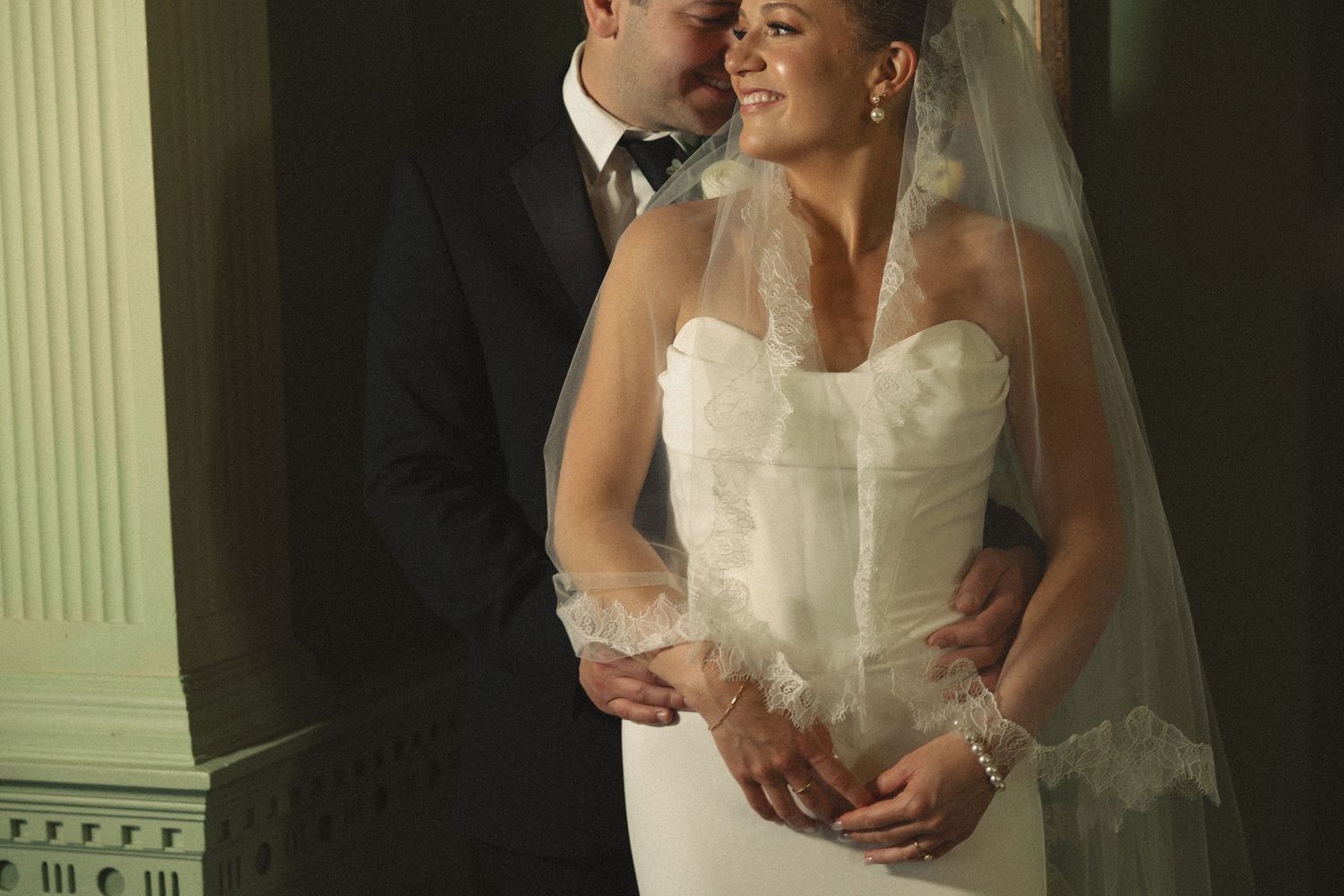 A romantic wedding portrait captured in soft lighting against classic white columns.