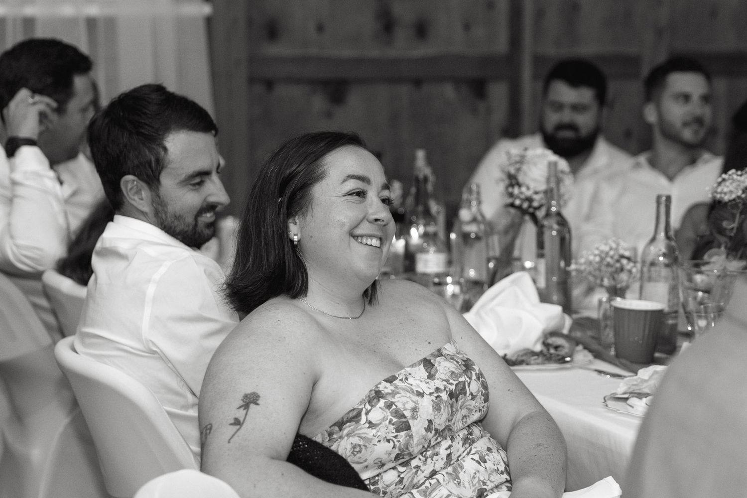 Wedding guests laugh and smile during reception dinner in rustic barn setting.